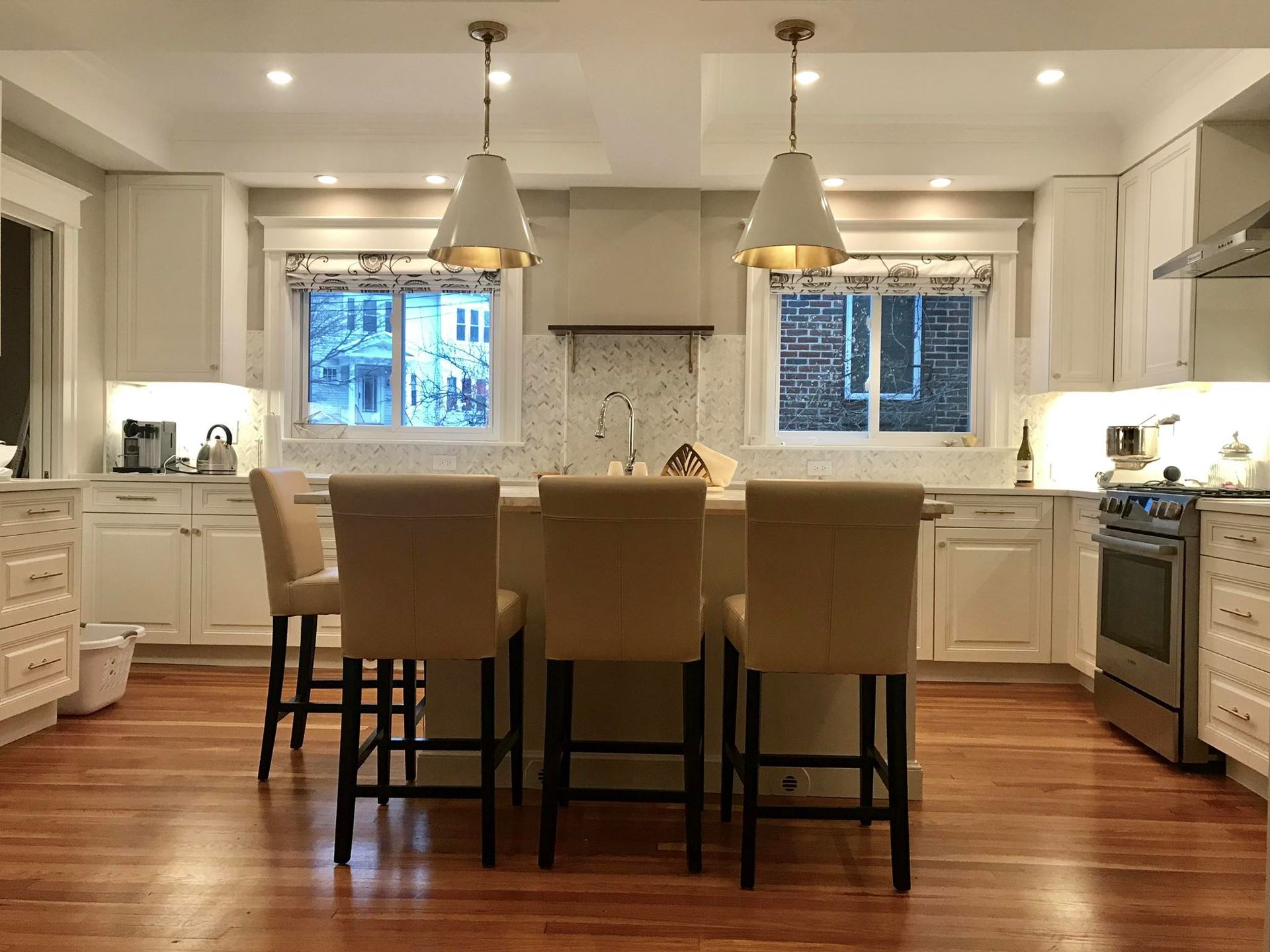 Bright white kitchen with island, two pendant lights, and tan bar stools on a wooden floor.