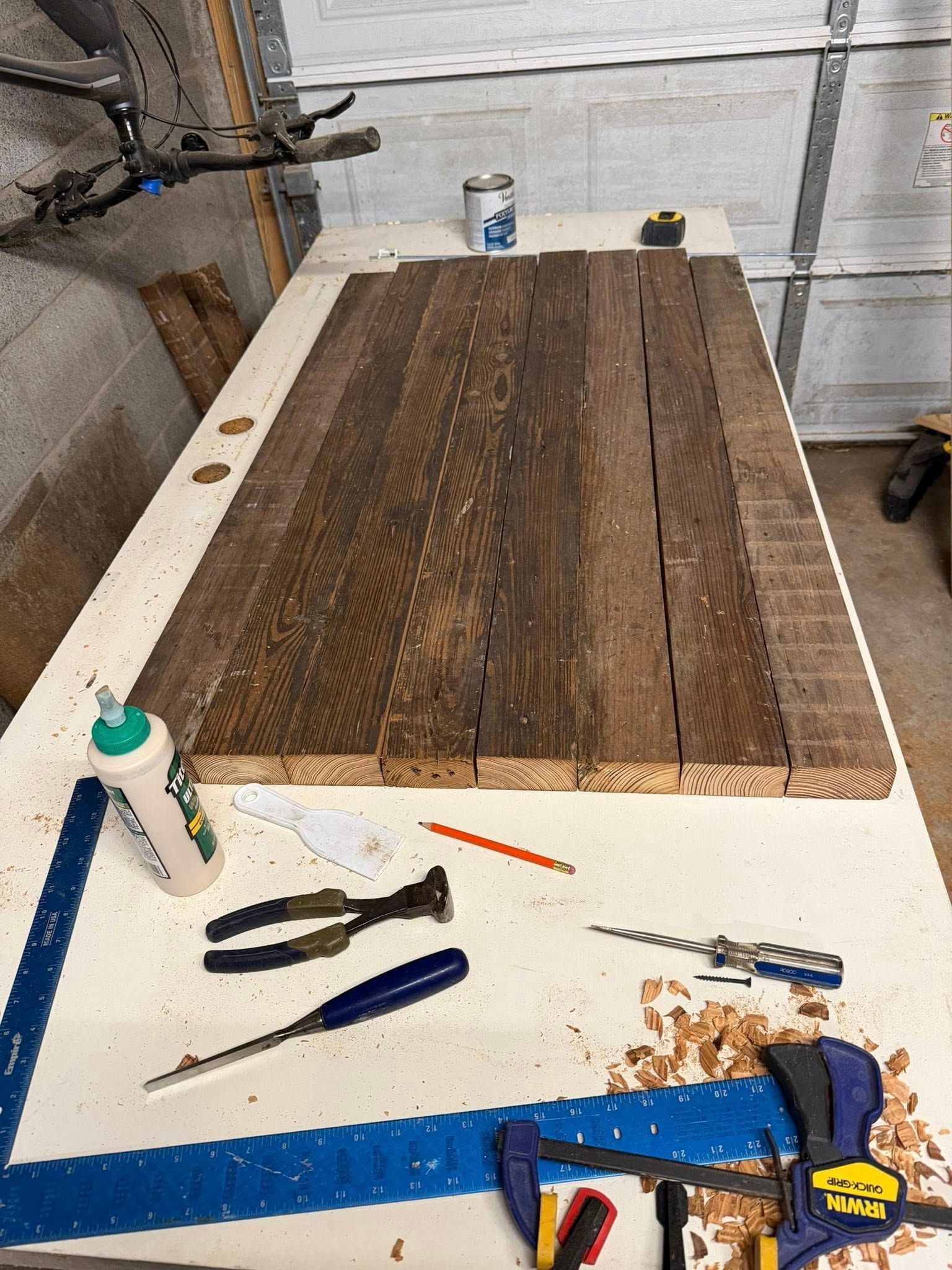 Workbench with a wood slab being sanded or refinished, surrounded by tools in a garage-like workshop.