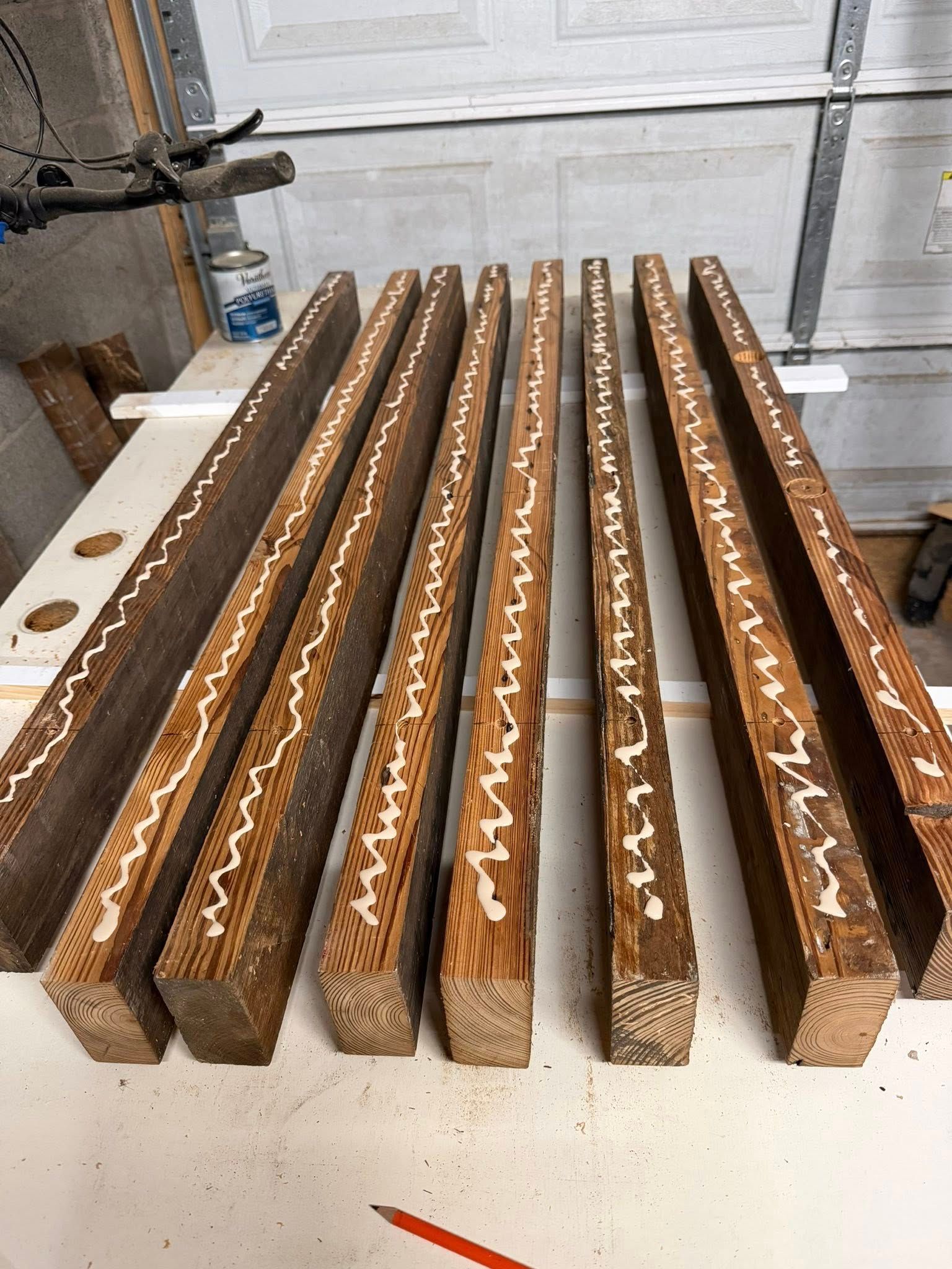 Several long wooden beams with zigzag edges lined up on a workshop table with white glue applied.