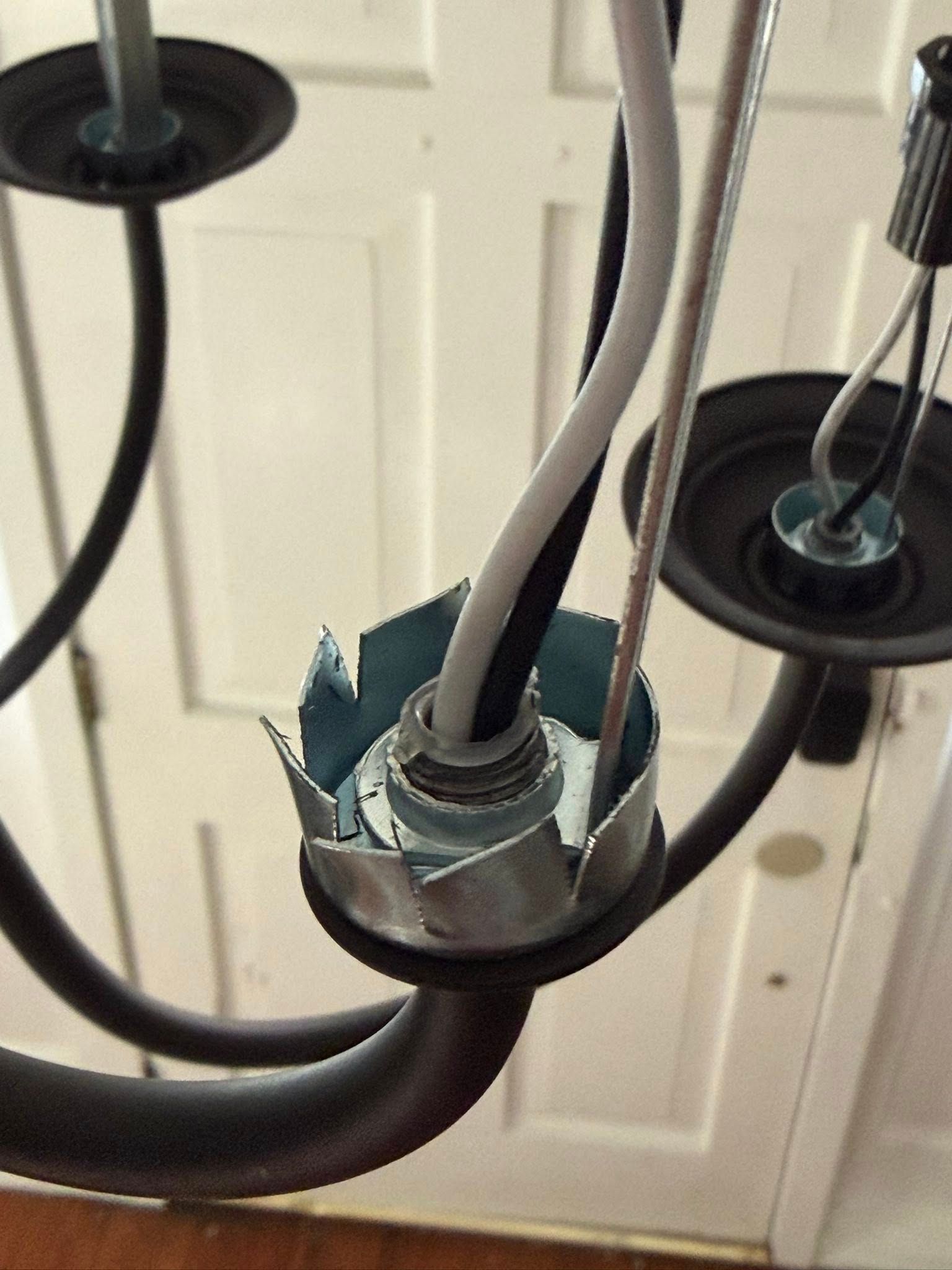 Close-up of a damaged black chandelier with exposed wiring against a white door backdrop