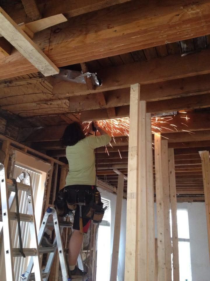 Worker using a power saw to cut overhead wood beams in a construction site room