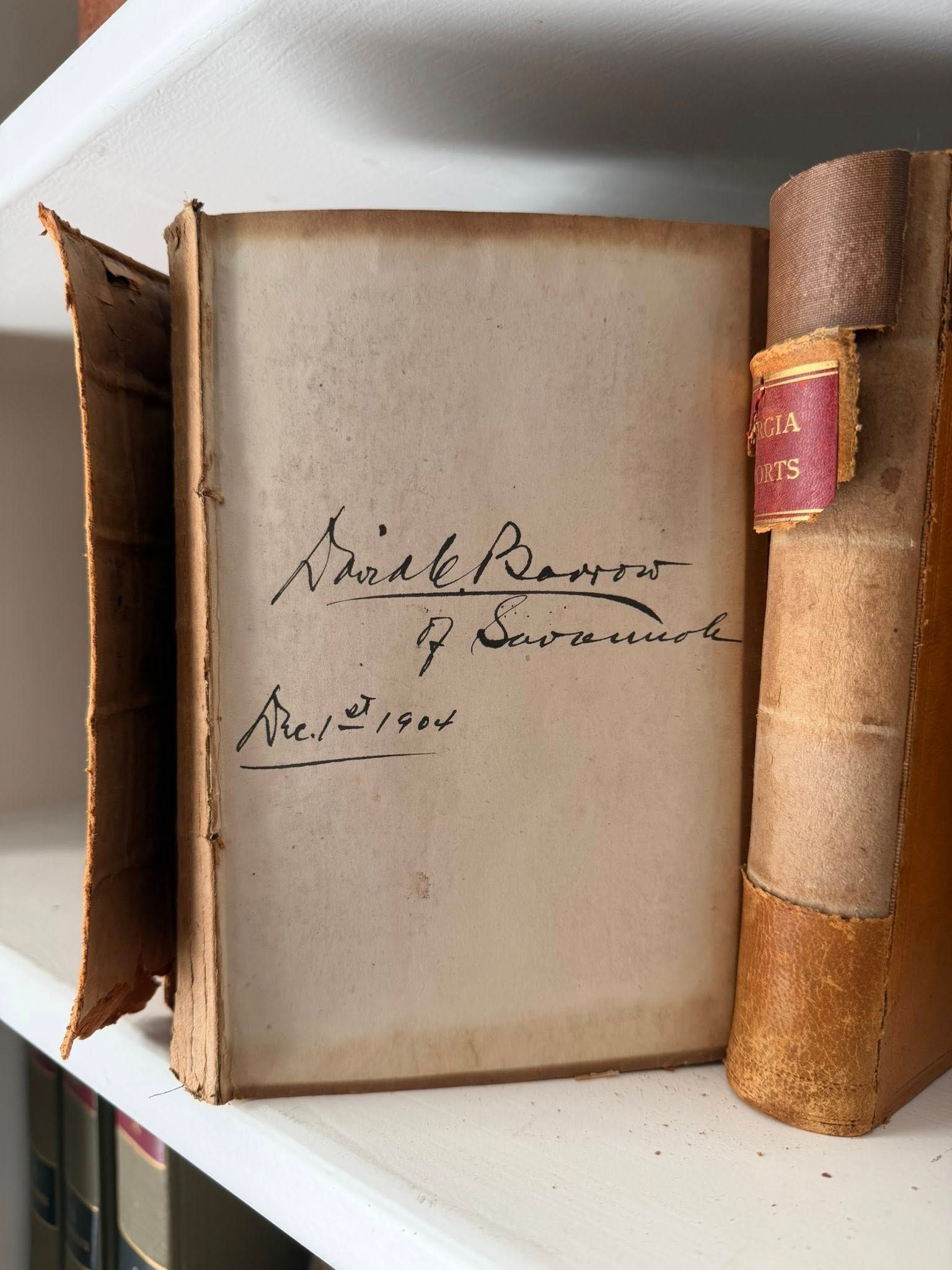 Old leather-bound book open on a shelf, showing a blank page with handwritten notes and a worn spine