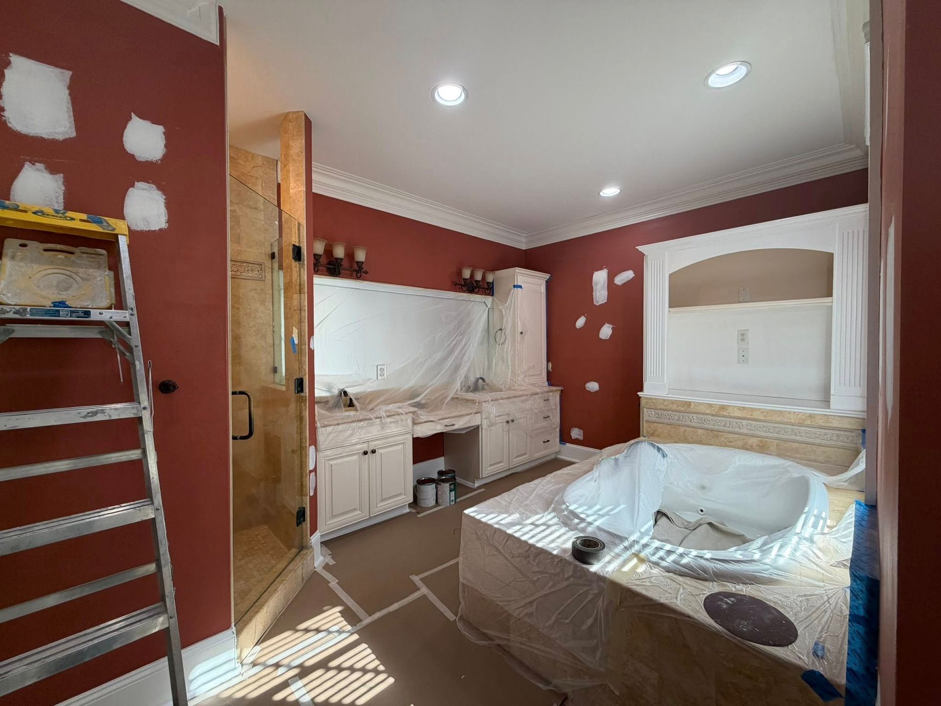 Bedroom with red walls, a bed, dresser, and a ladder against the wall, seen in mid-renovation.