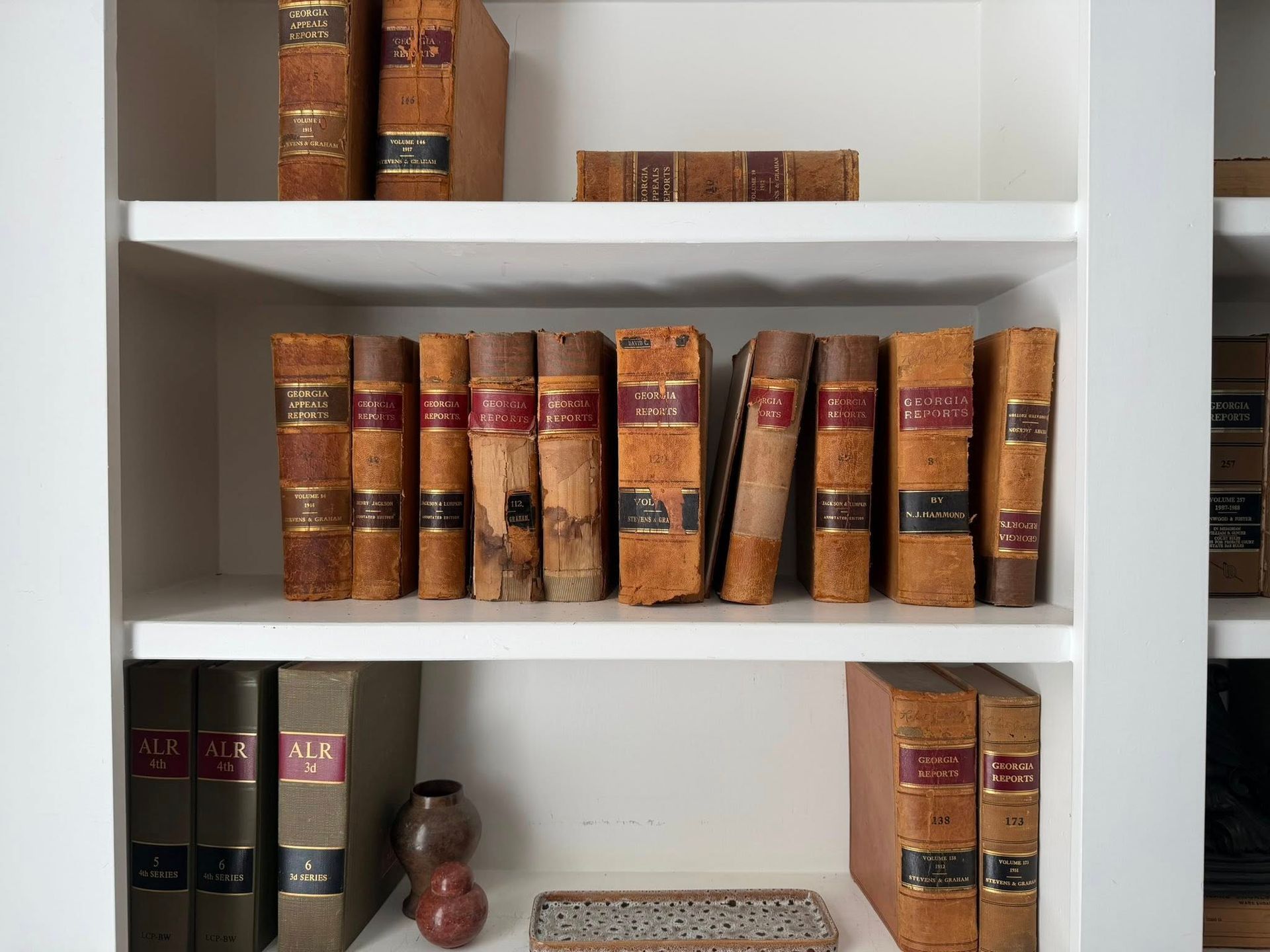 White bookshelf with rows of old leather-bound books and a small decorative statue on the bottom shelf