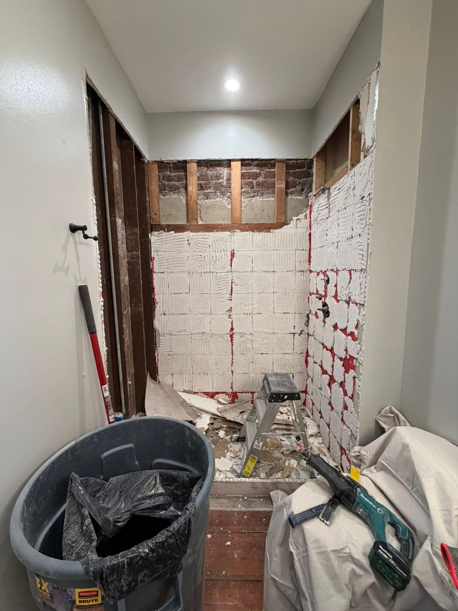 Narrow hallway under renovation with exposed walls, construction debris, and tools scattered on the floor