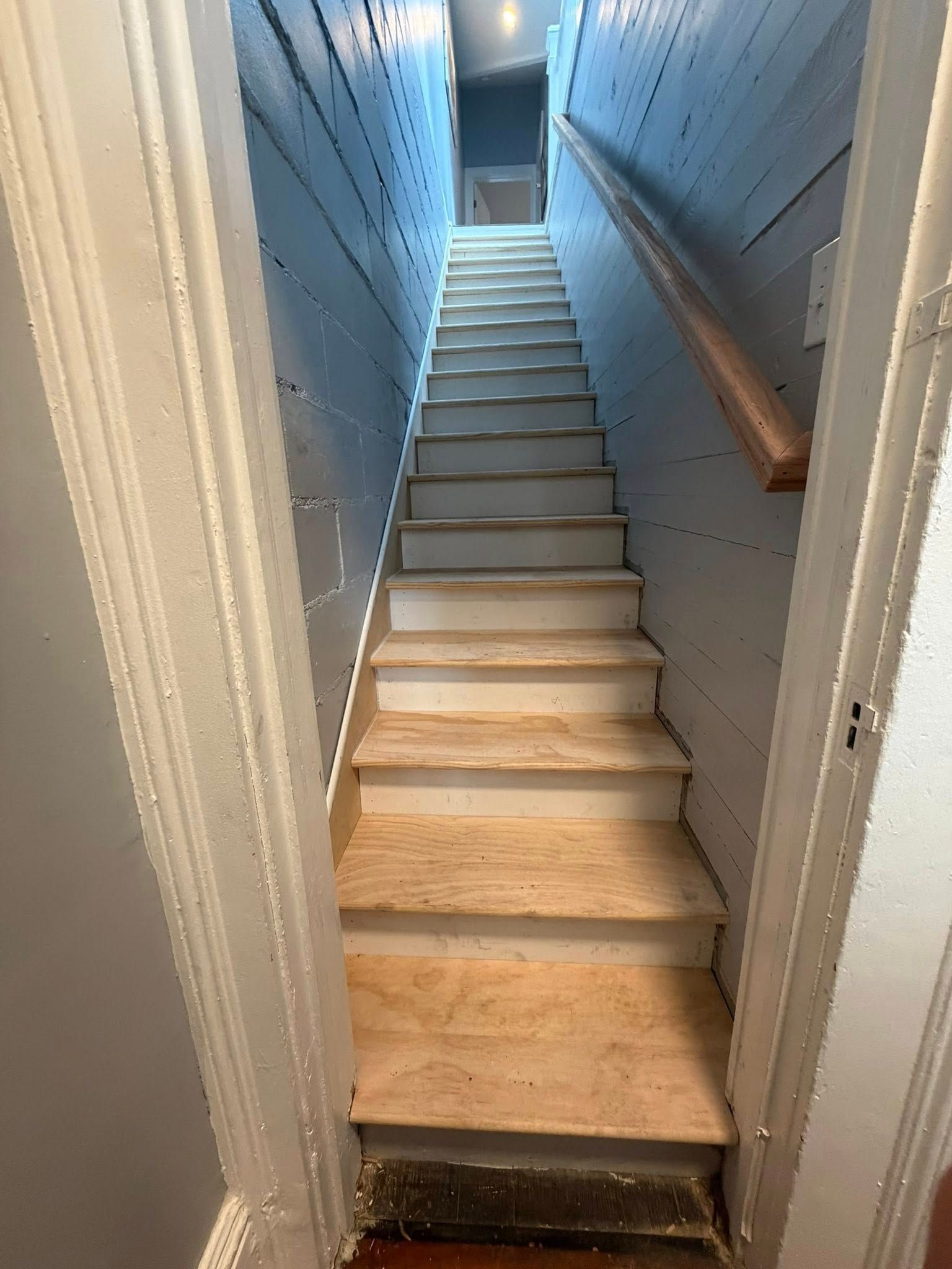 Narrow unfinished stairwell with plywood steps and blue walls leading upward