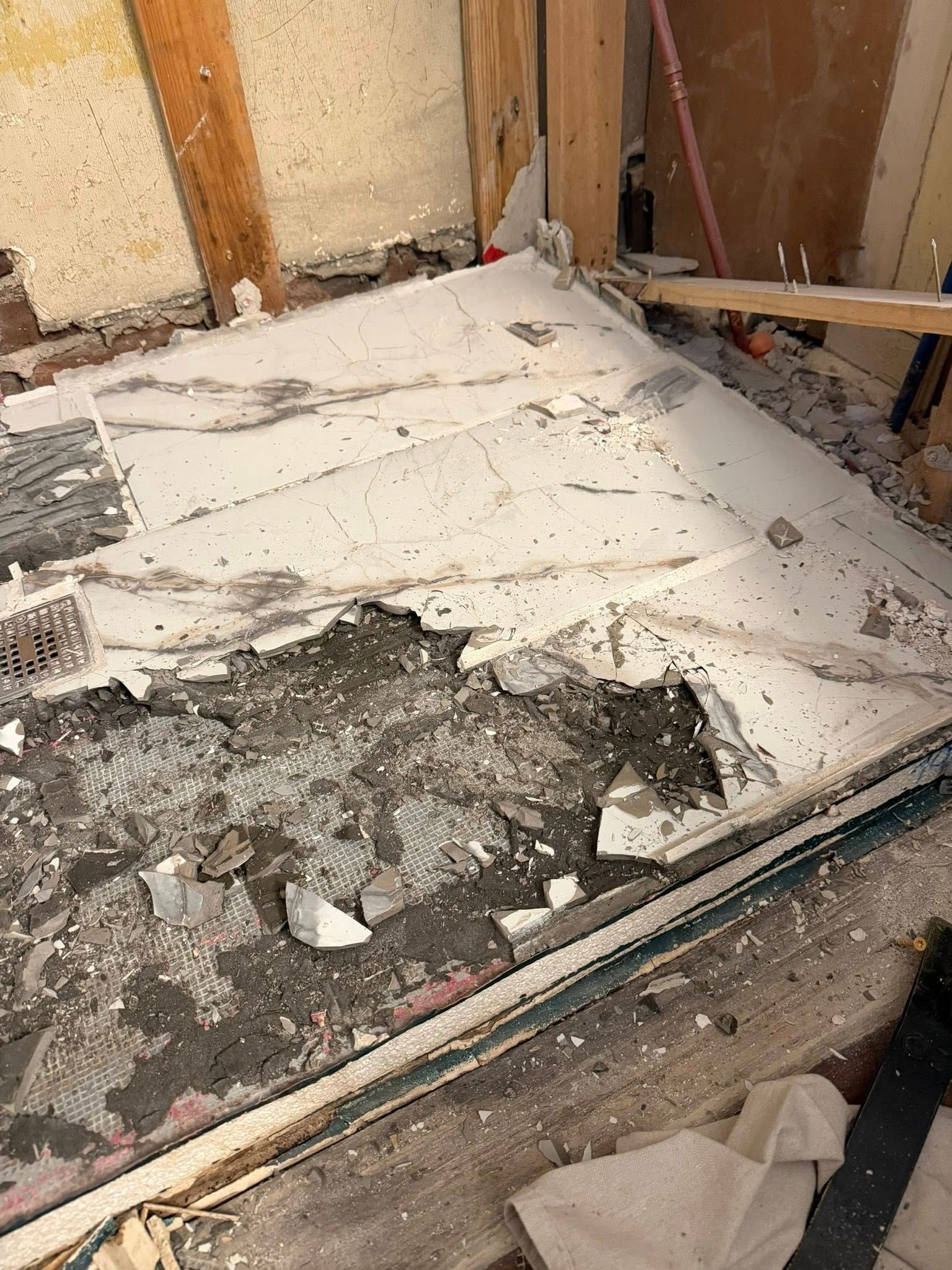 Damaged floor with broken white material and rubble inside an unfinished wall corner