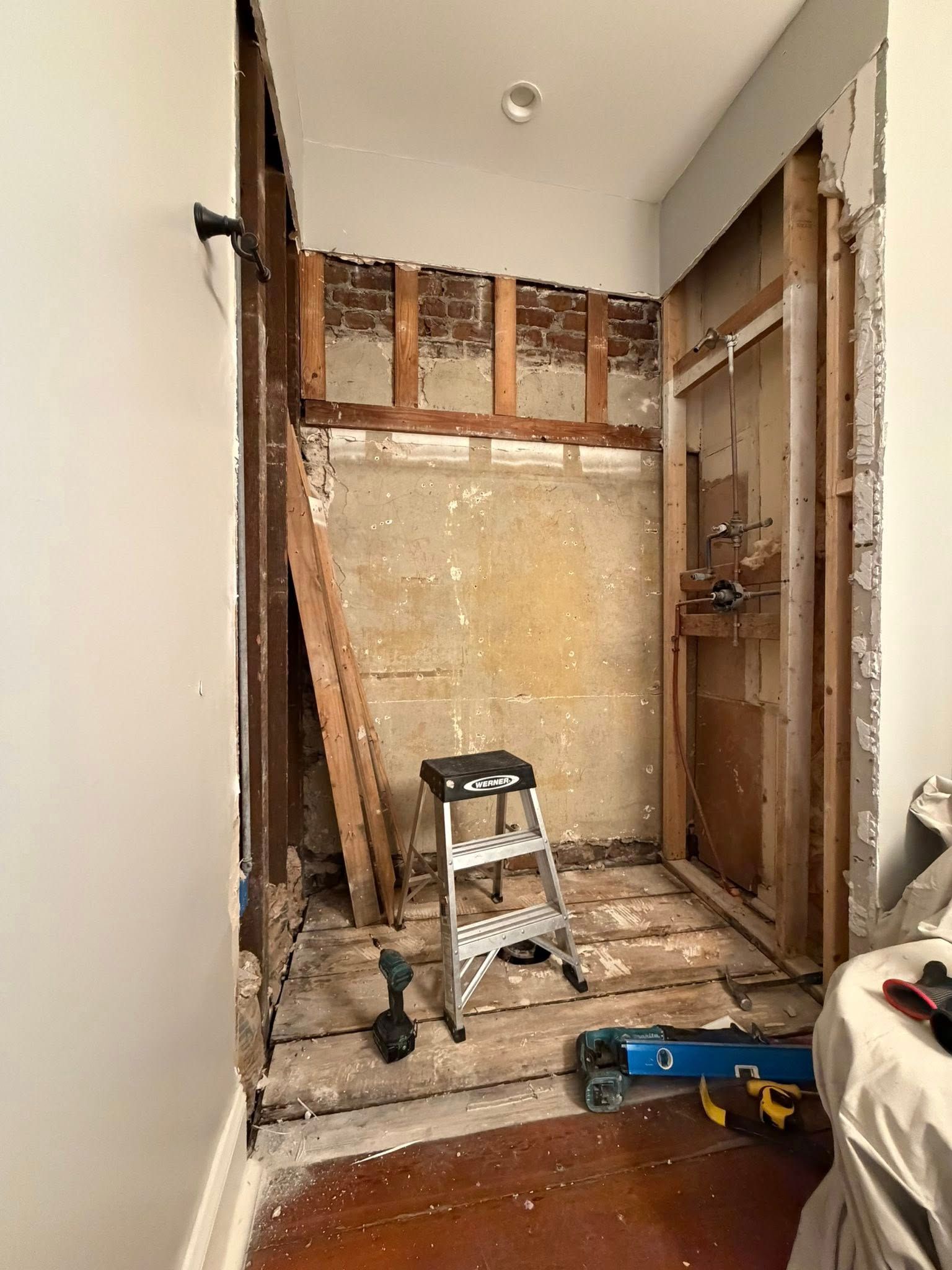 Small room under renovation with exposed wall studs, ladder, and construction tools on the floor.