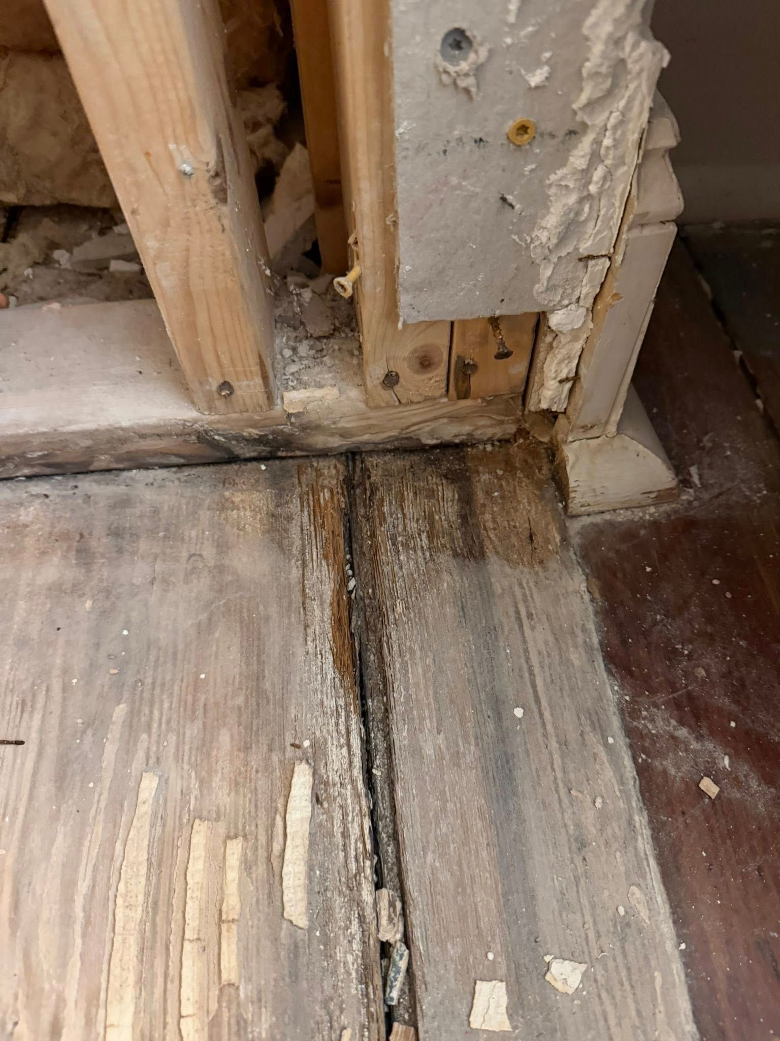 Damaged wooden floor and wall corner with gaps, peeling paint, and visible water stain