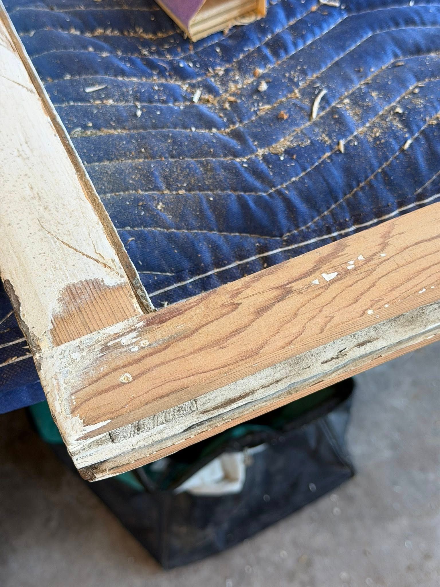 Close-up of a damaged wooden frame with peeling white paint and a blue quilted cushion underneath.