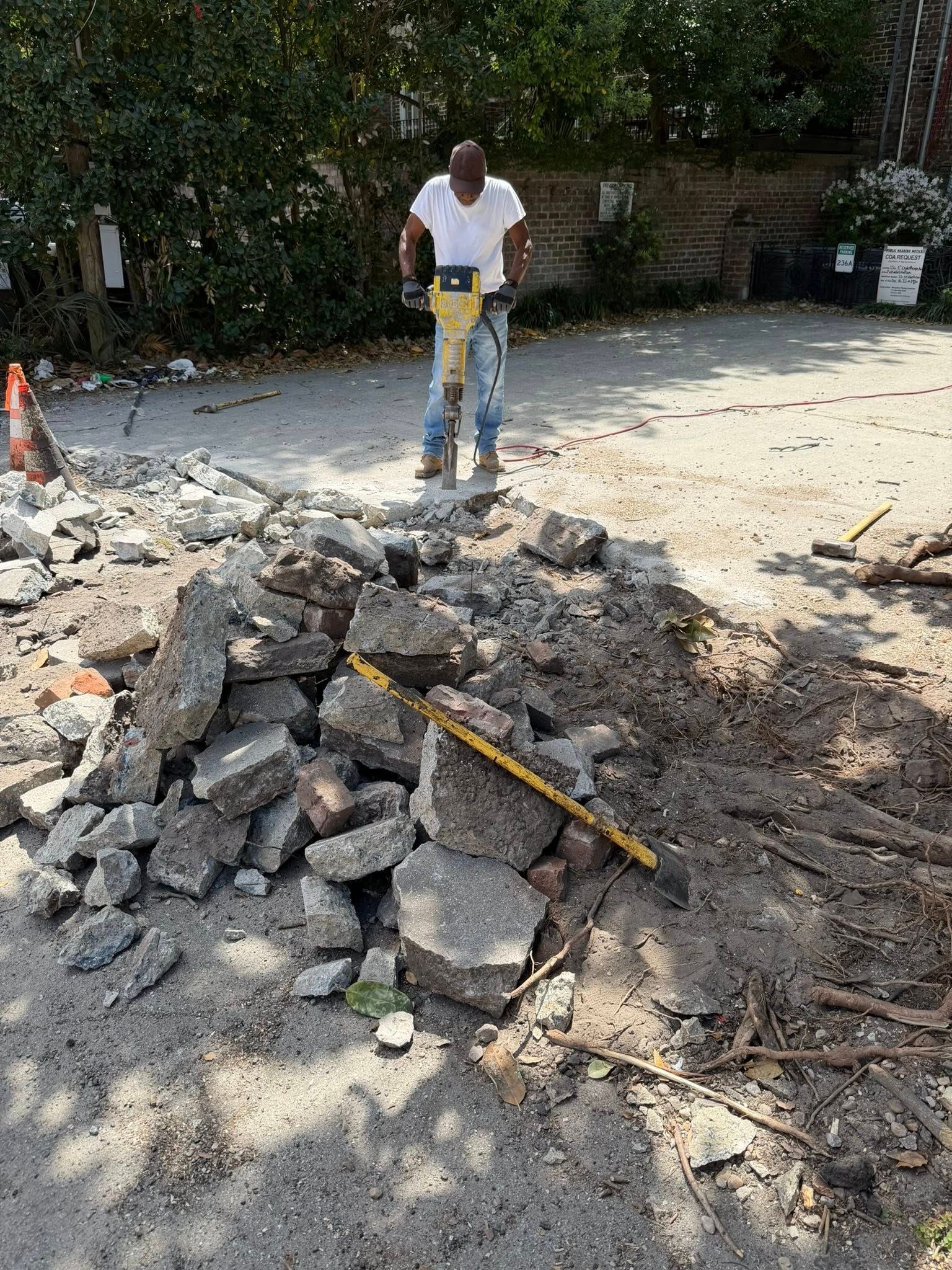 Worker standing beside a pile of broken asphalt and rubble on a road construction site.