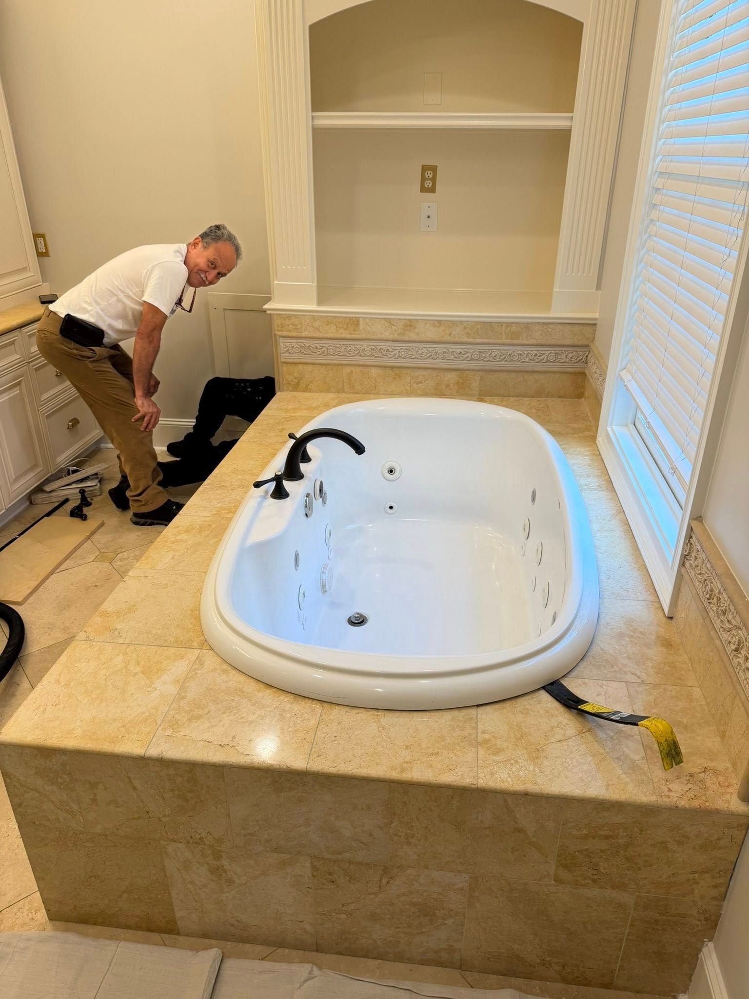 Man working on a built-in bathroom tub with cream stone surround and shelves