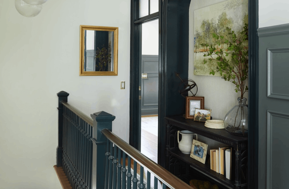 Hallway with dark stair railing, wall mirror, and black cabinet holding books and decor.