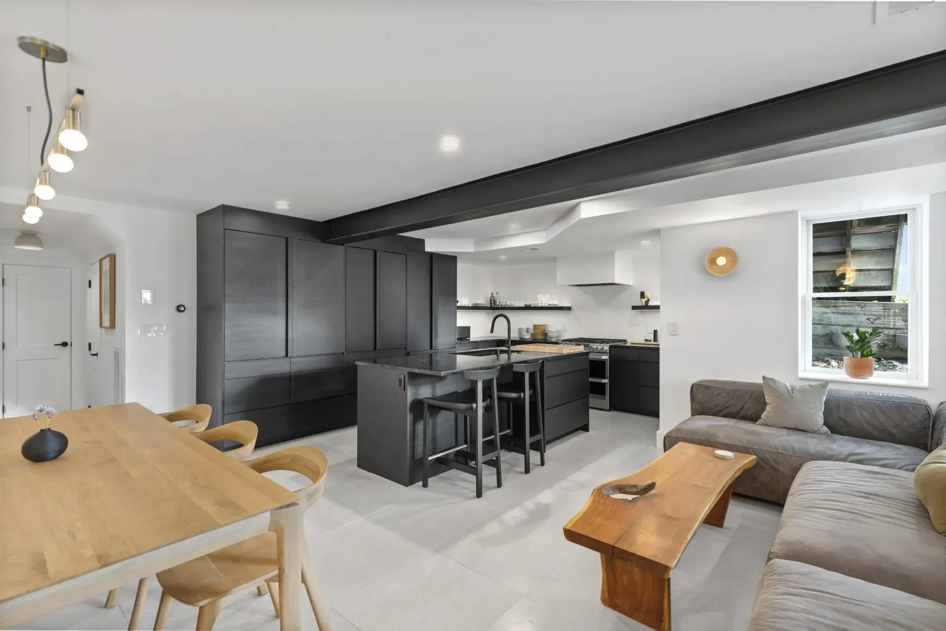 Modern open-concept living room and kitchen with gray sofa, wood table, and dark cabinets