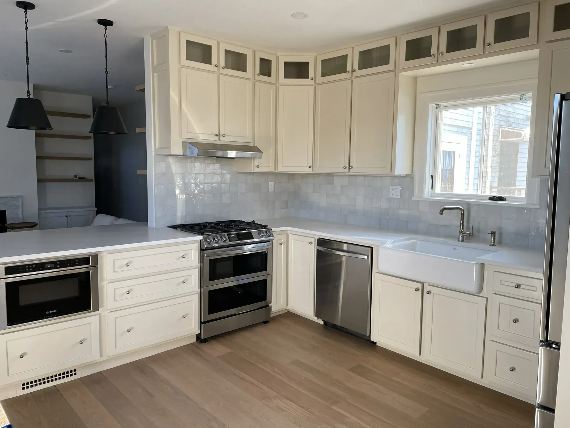 Bright white kitchen with wood floors, stainless steel appliances, and a large window over the sink.