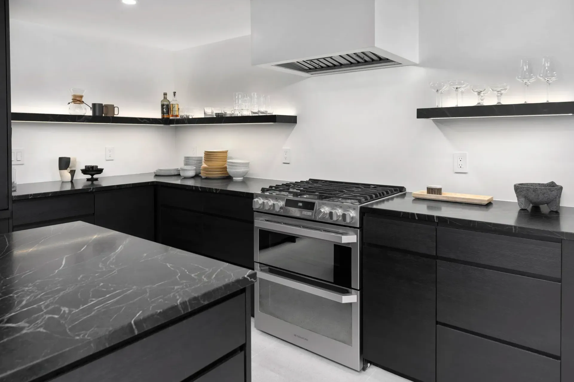 Modern black-and-white kitchen with marble countertops, gas range, open shelves, and minimalist decor