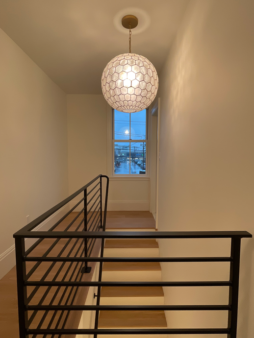 Narrow stairwell landing with black railing, hanging globe light, and a small window at the end.