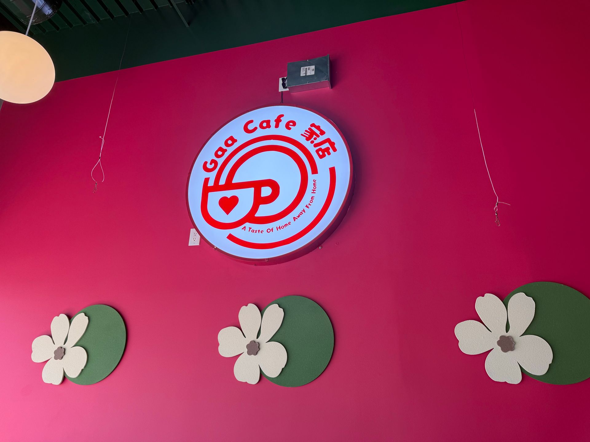 Pink Cafe logo sign on a wall with flower decorations on a pink and green background