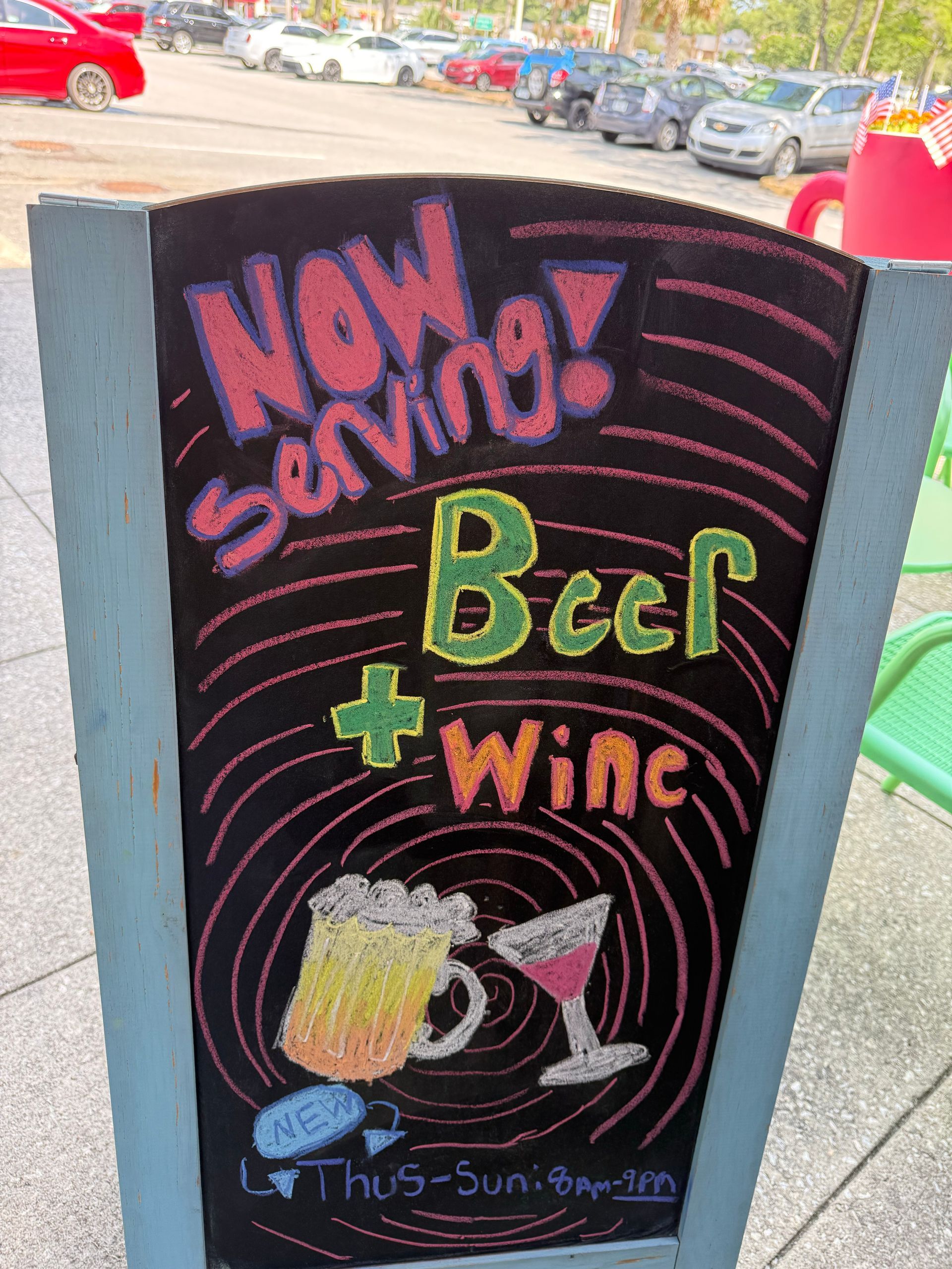 Chalkboard sidewalk sign advertising “Now Serving! Beer + Wine” with beer mug and wine glass drawings.