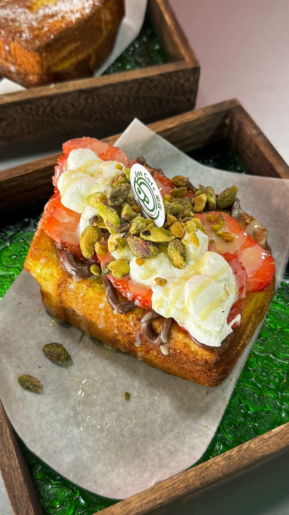 Berry-topped dessert bars with cream and pistachios in wooden trays on green garnish