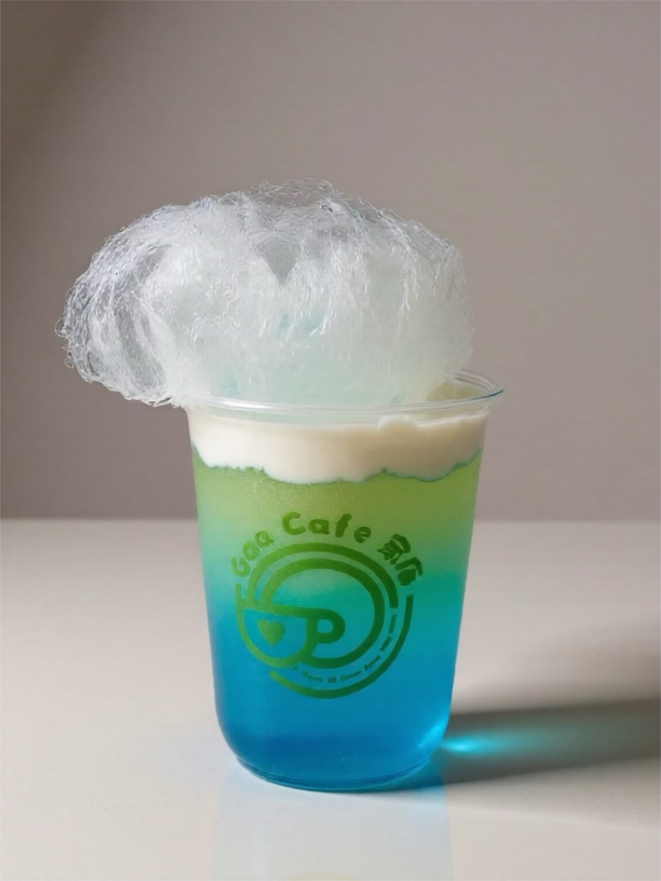 Blue-and-green drink in a clear cup topped with fluffy white cotton candy
