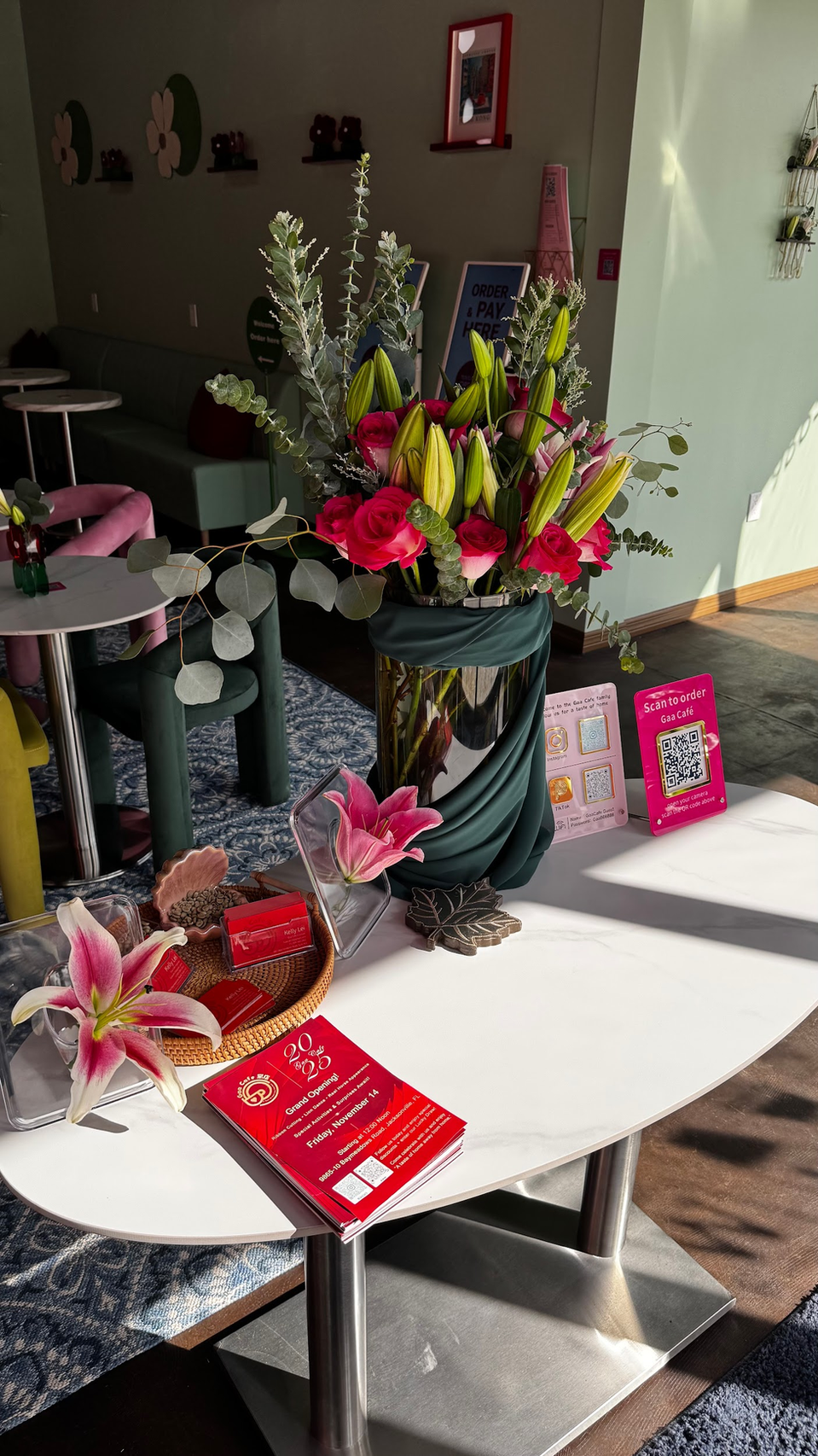 Flower arrangements on display in a sunlit room, with red cards on white tables and a decorated gift basket.