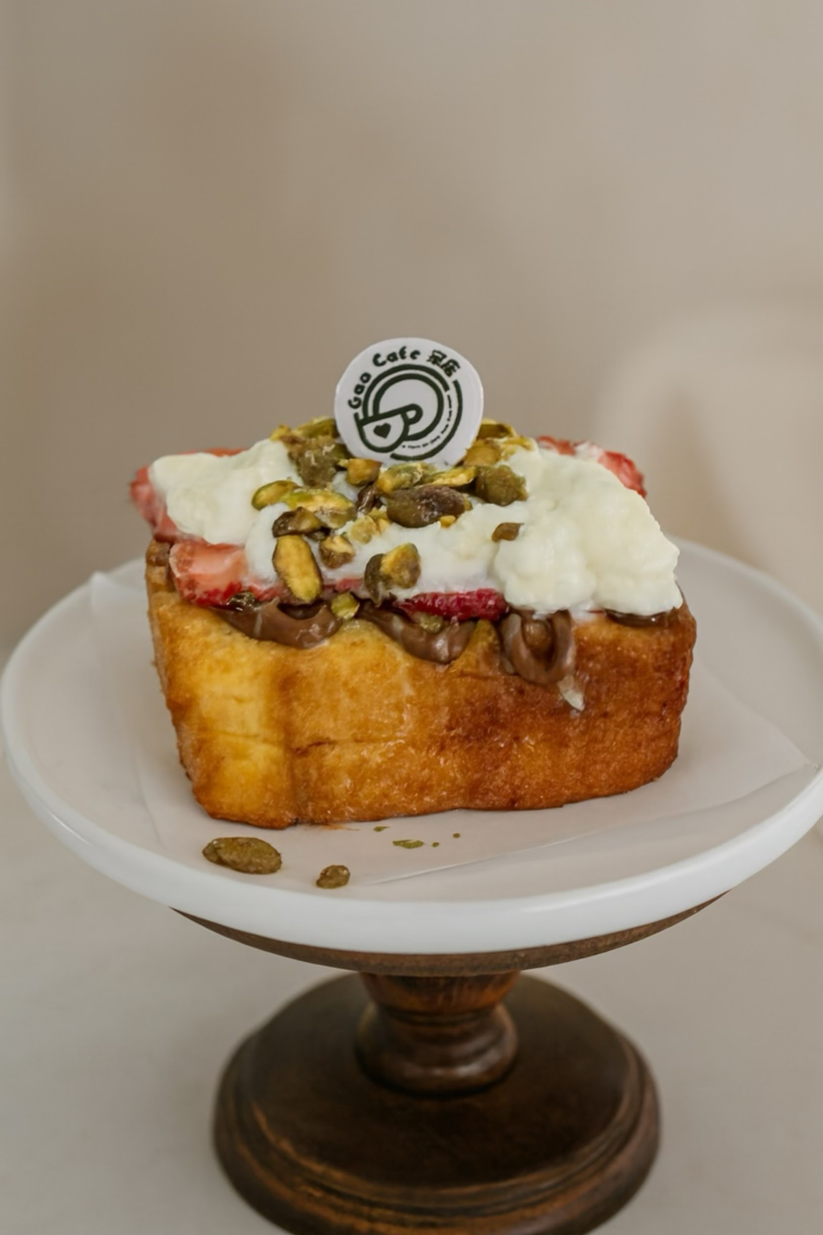 Pastry topped with cream and pistachios on a white pedestal plate