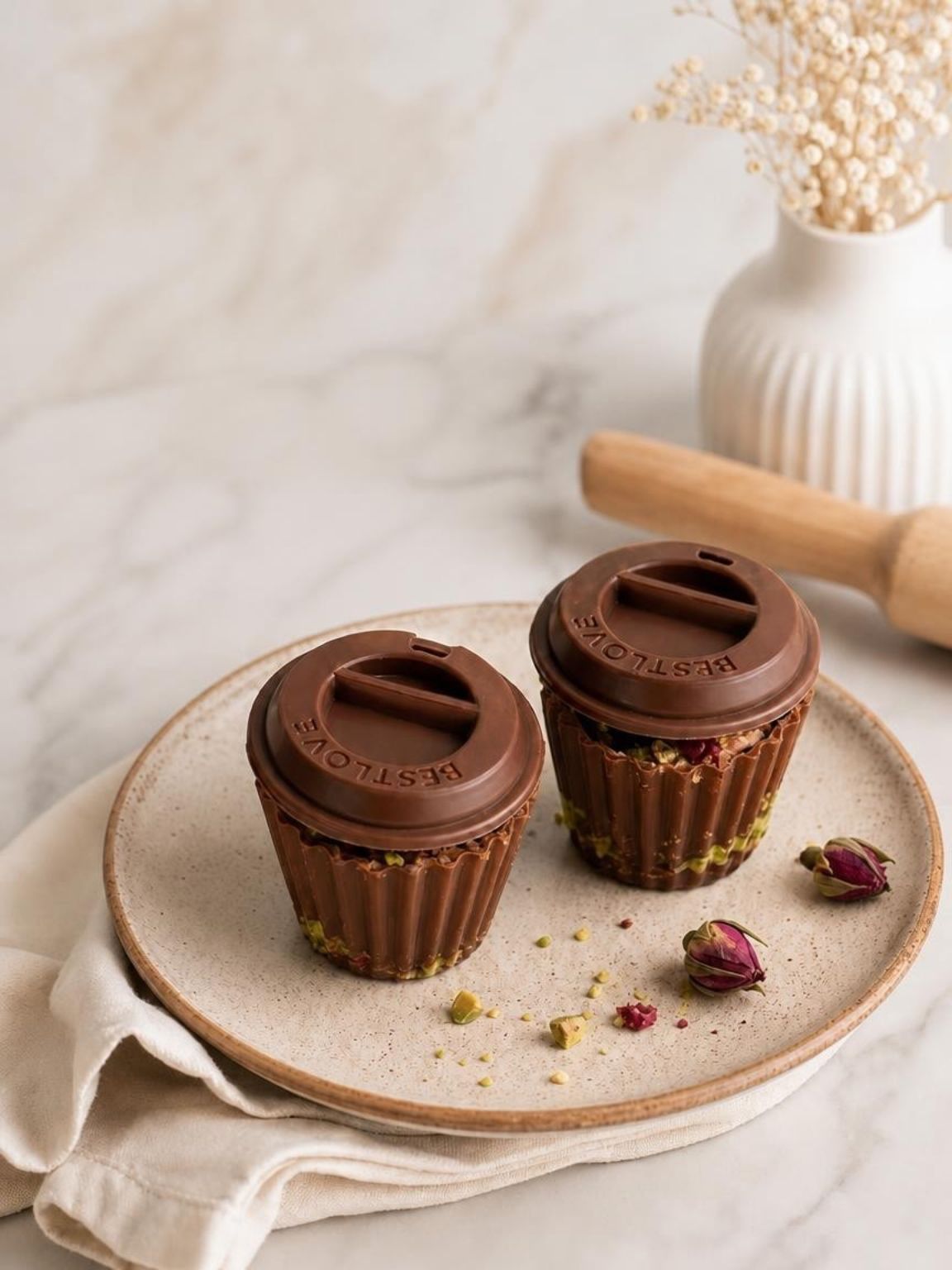 Two chocolate cupcakes on a plate with a marble backdrop, wooden rolling pin, and dried flowers