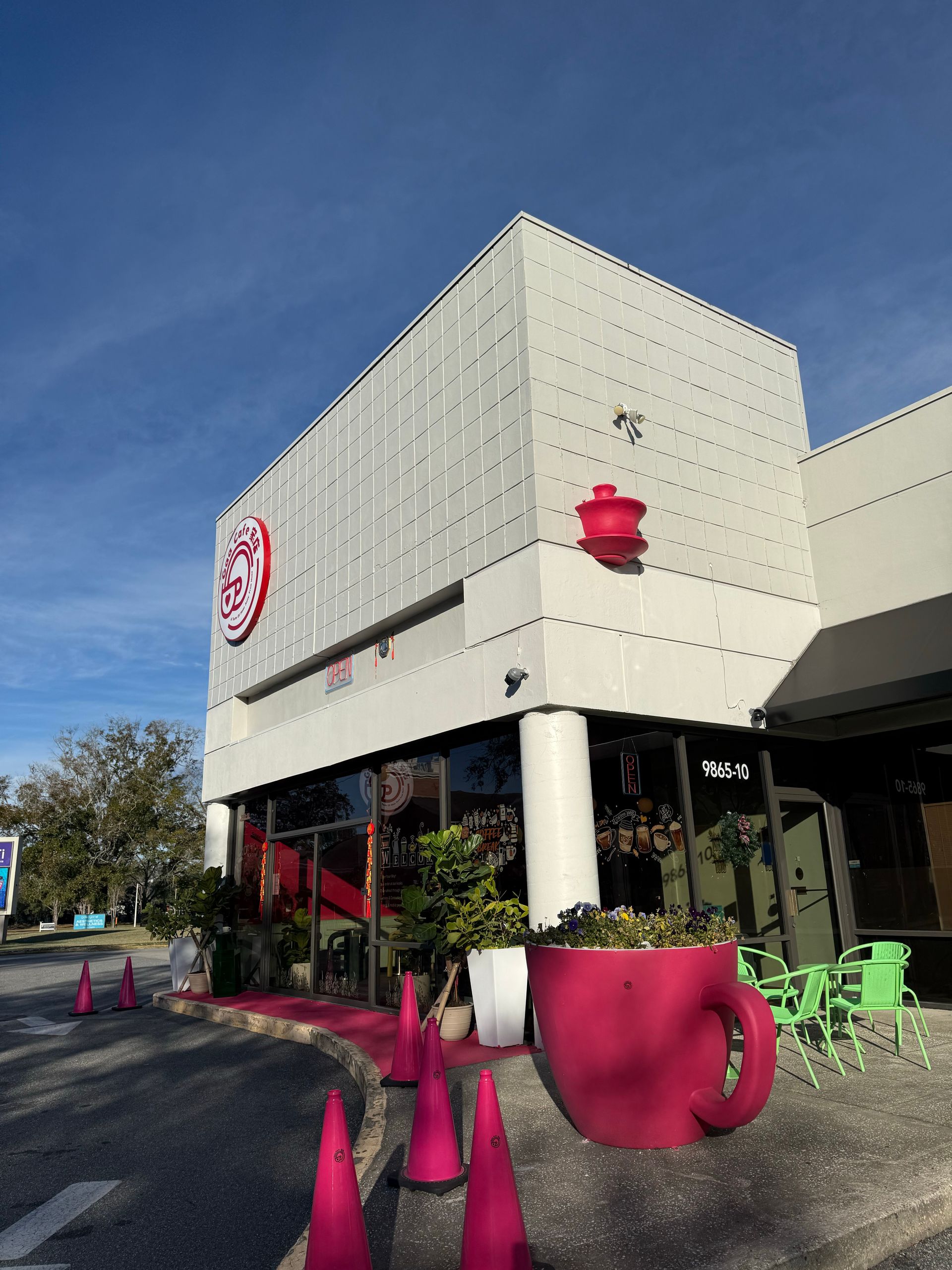 Outdoor café with bright pink chairs and cones outside a modern white building under a blue sky