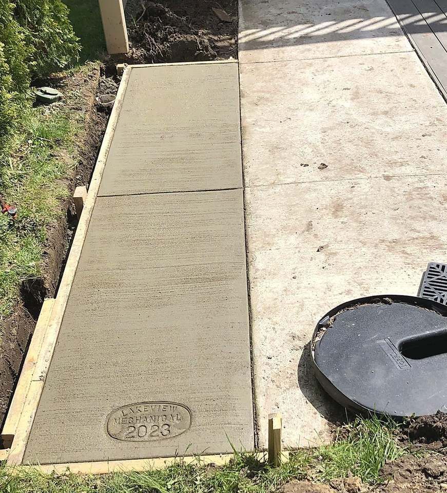 New concrete walkway stamped Lakeview Mechanical 2023, poured after a Lakeview sewer dig