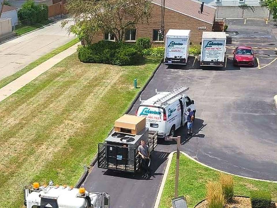Lakeview Mechanical vans and a new rooftop unit on a trailer below a crane on a commercial job