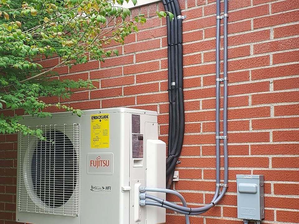 Fujitsu ductless mini-split outdoor unit mounted on a brick wall with covered line sets, installed by Lakeview