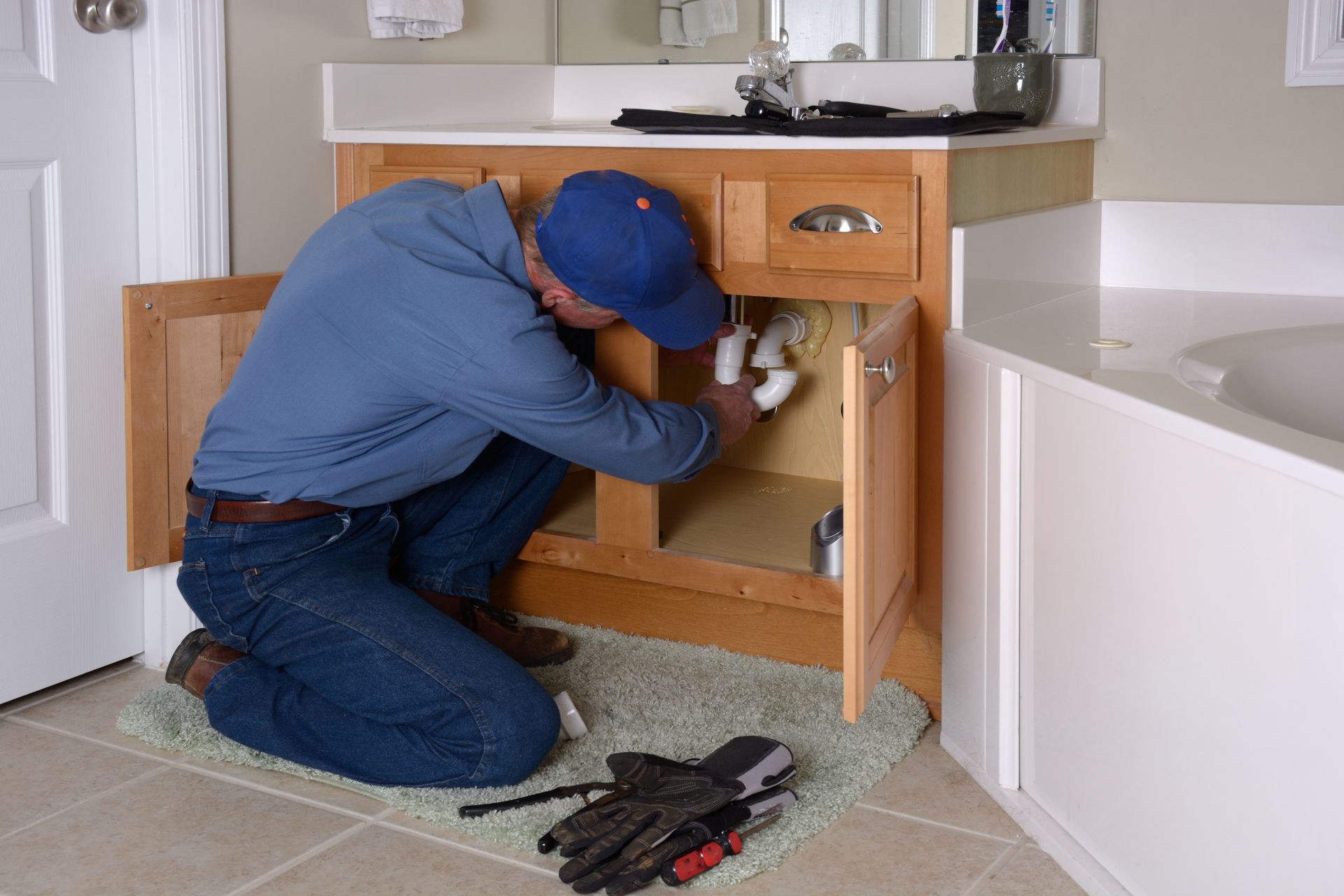 Plumber performing drain cleaning services under a bathroom sink in Warren, MI