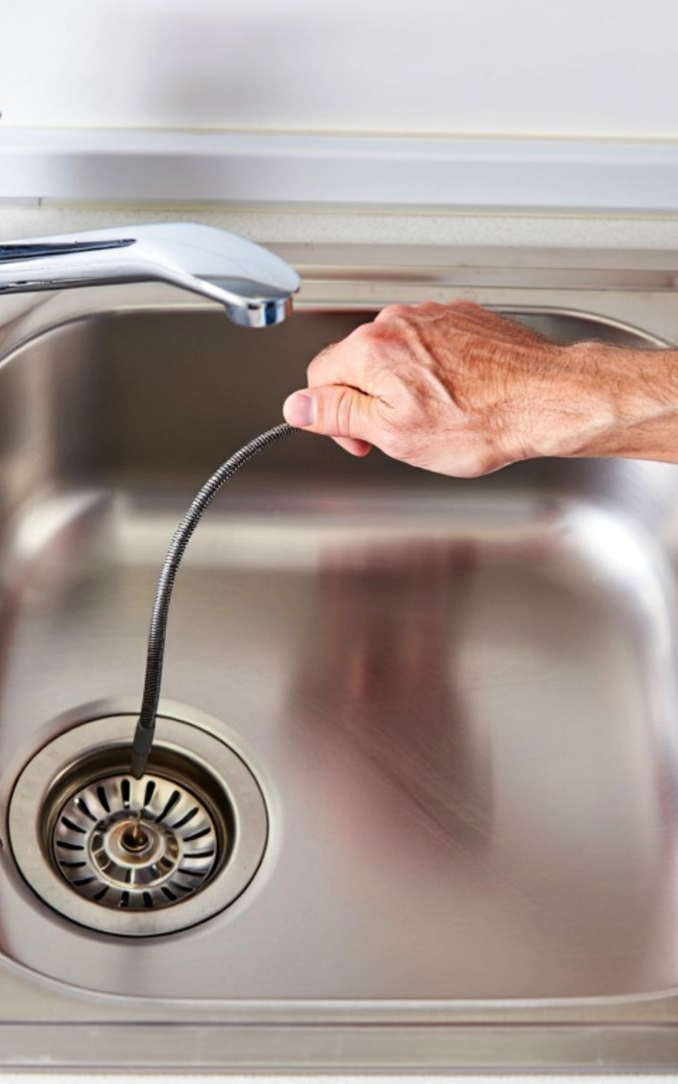 An experienced plumber clearing a clogged kitchen sink drain with specialized equipment.