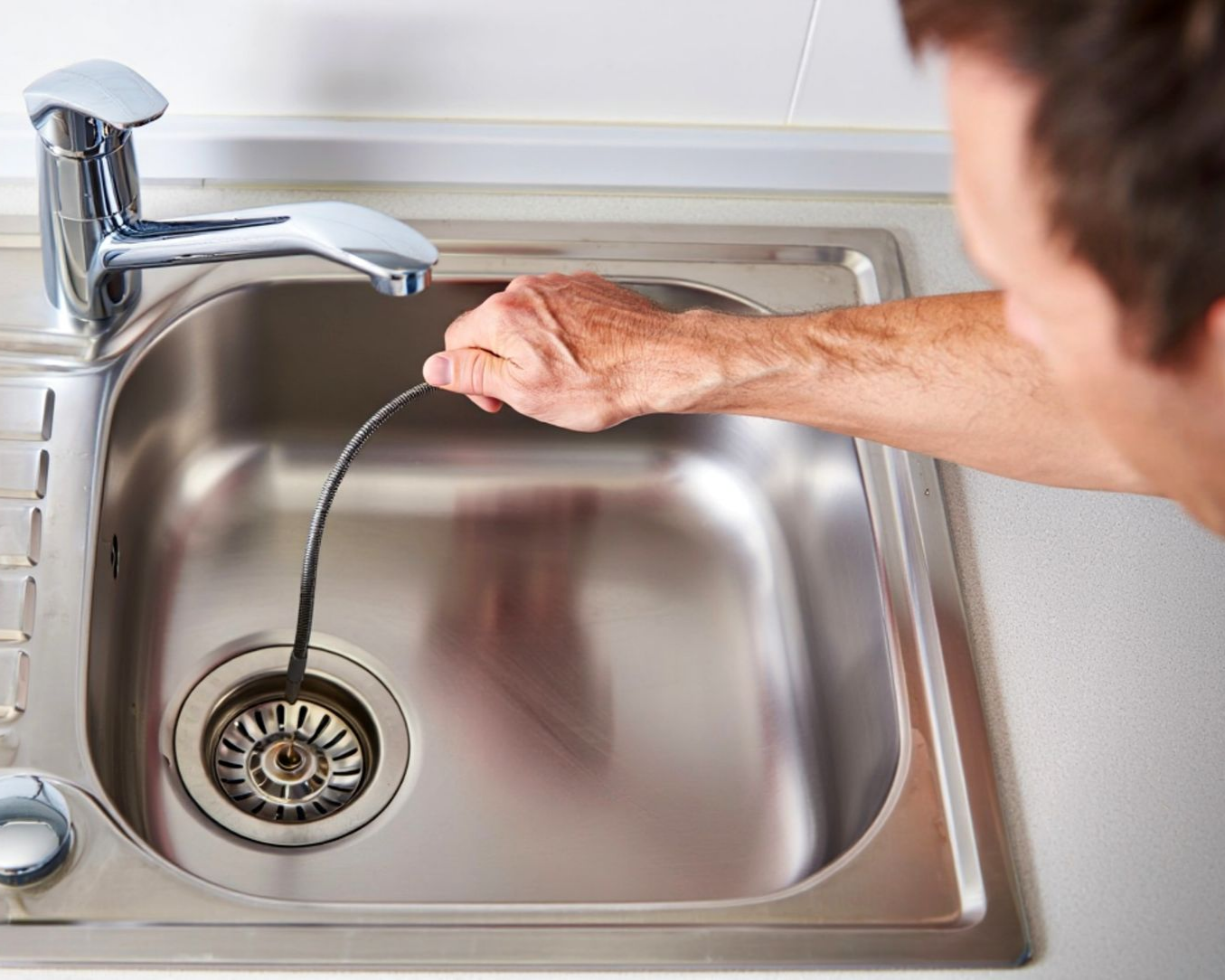 An experienced plumber clearing a clogged kitchen sink drain with specialized equipment.