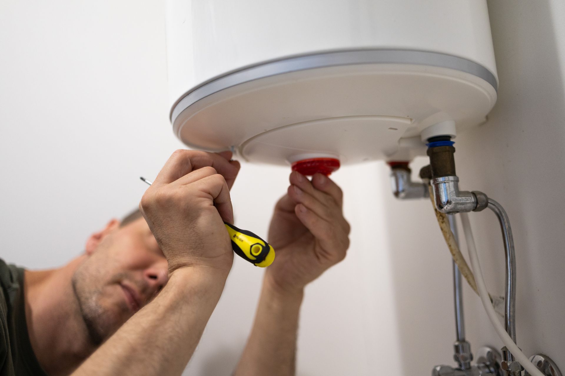 Plumber using a yellow screwdriver during an electric water heater repair service. Plumber using a yellow screwdriver during an electric water heater repair service.