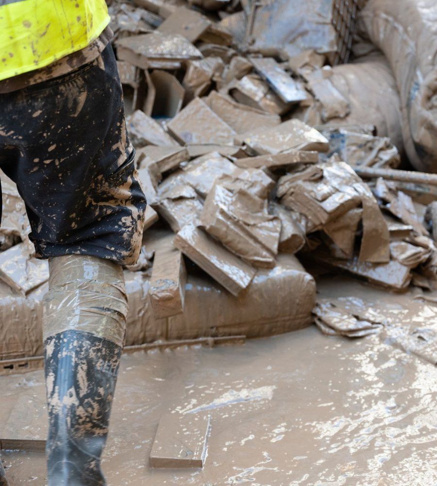 Worker in boots and a hi-vis vest standing in mud and debris left behind by flooding