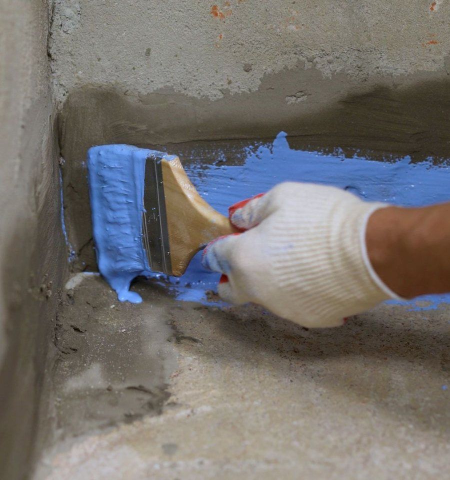 Gloved hand brushing waterproofing sealant onto a concrete foundation wall