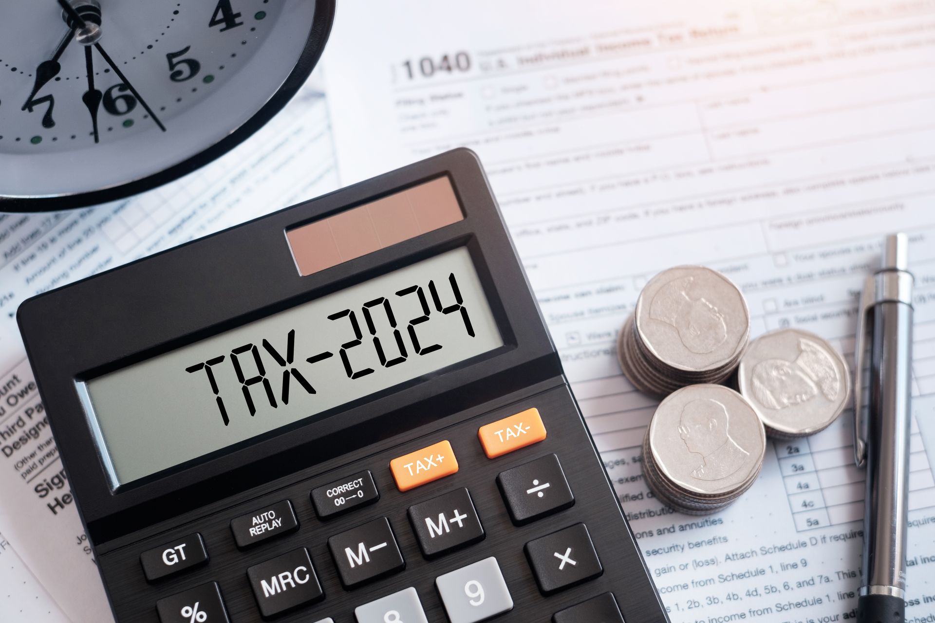 A calculator is sitting on top of a tax form next to coins and a pen.