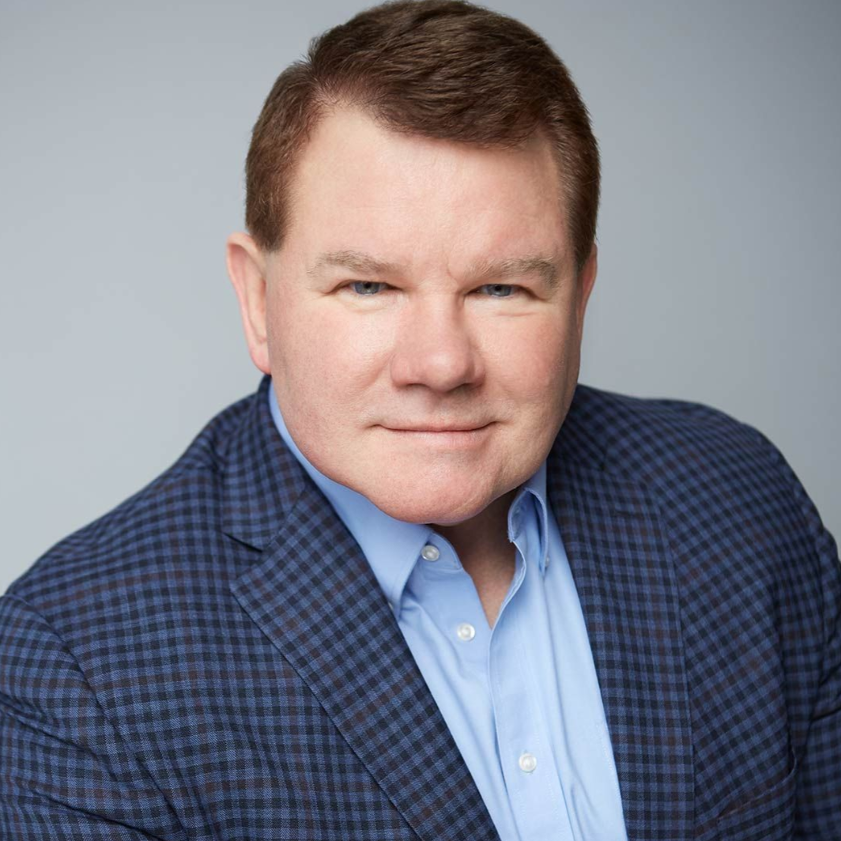 Headshot of a man in a blue checkered blazer and light blue shirt against a gray background