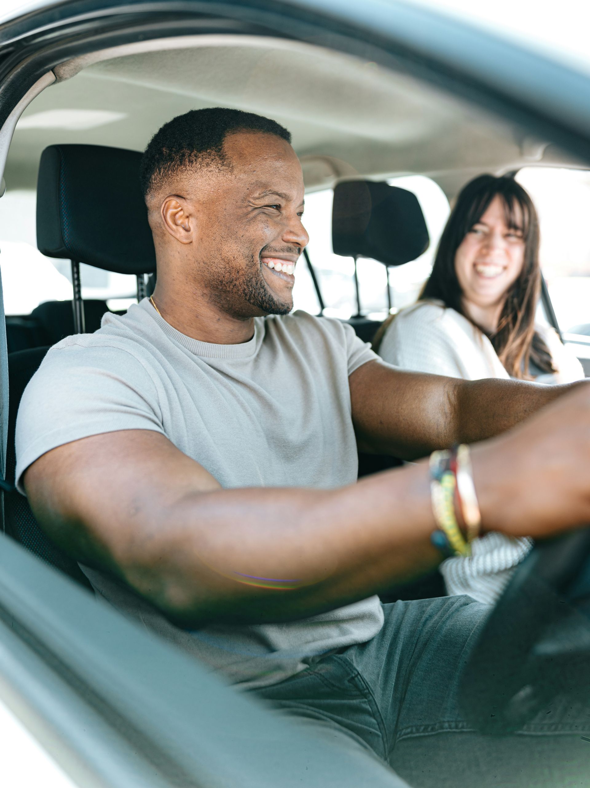 Two people smiling in a car, with the driver in the foreground and a passenger in the back seat