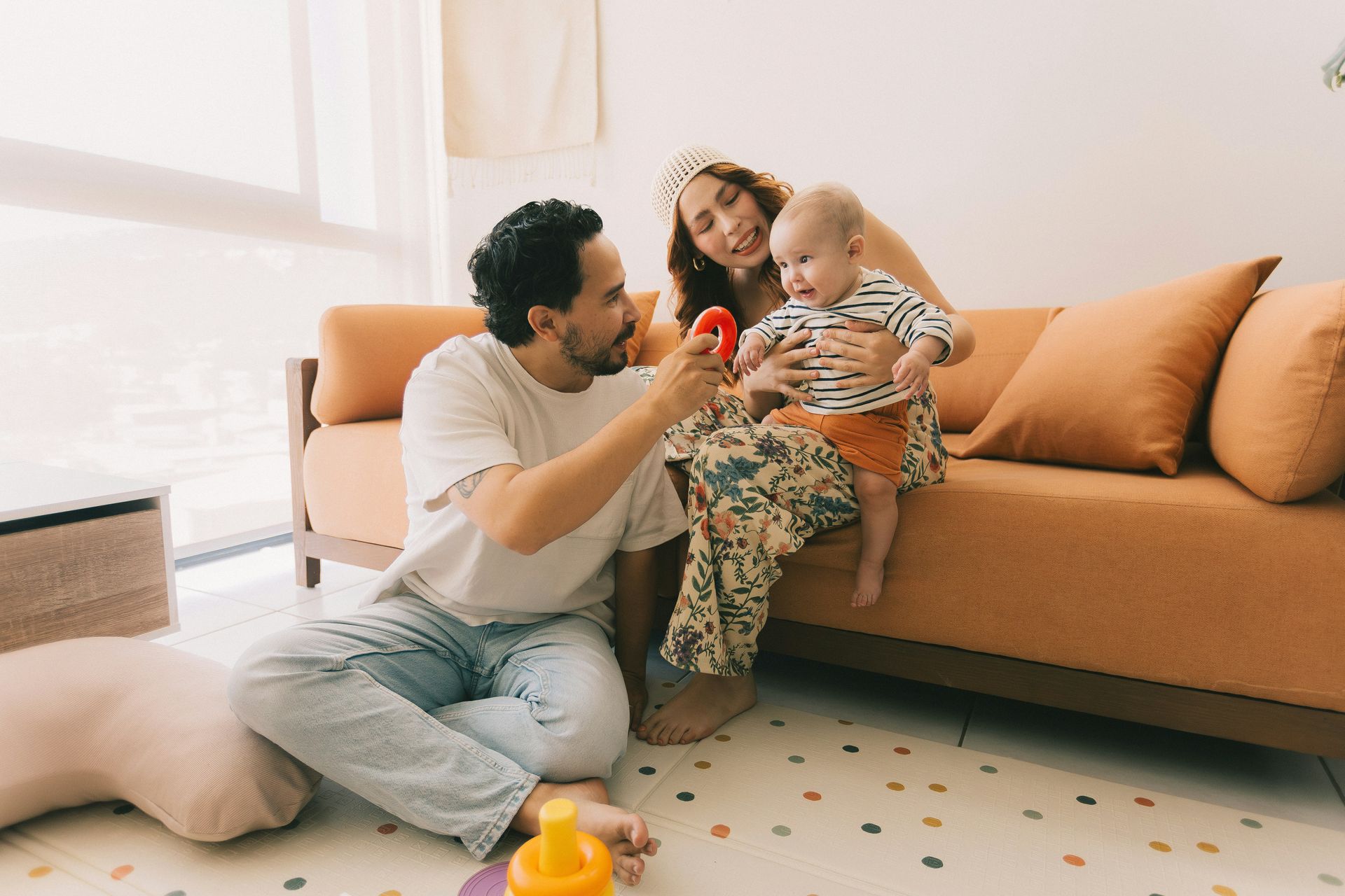 Family sitting on an orange couch, playing with a baby in a bright living room