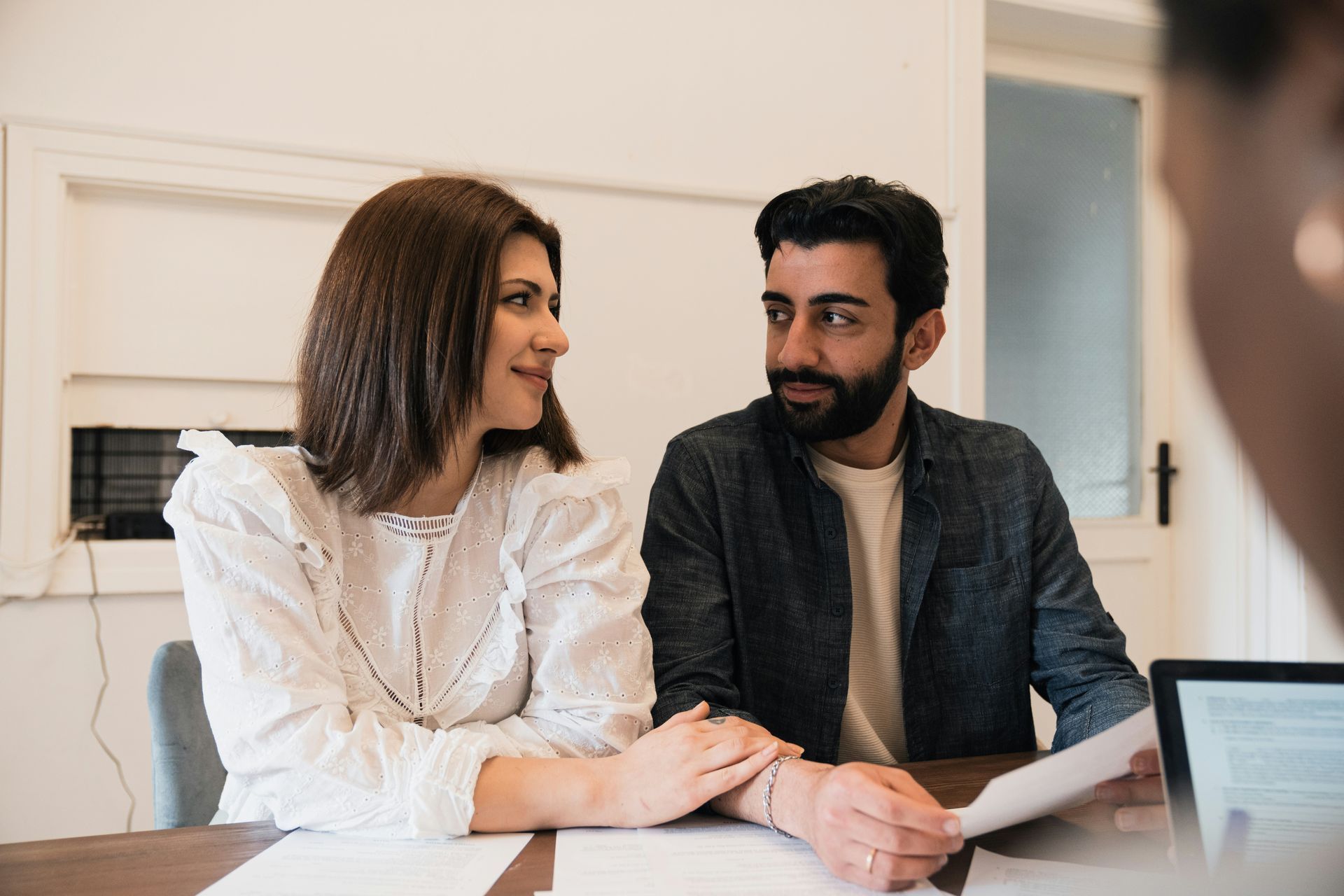 Two coworkers smiling and talking at a desk with a laptop in a bright office