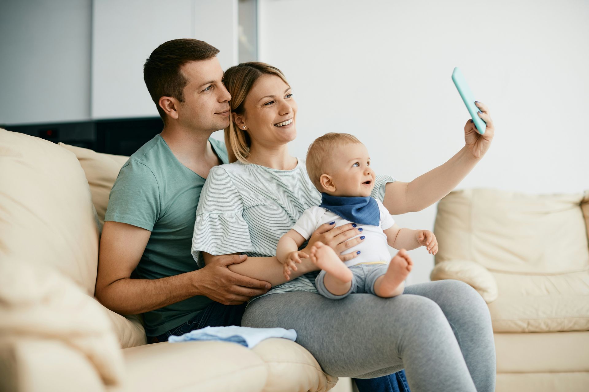 Family sitting on a couch, smiling for a selfie with a baby in the middle