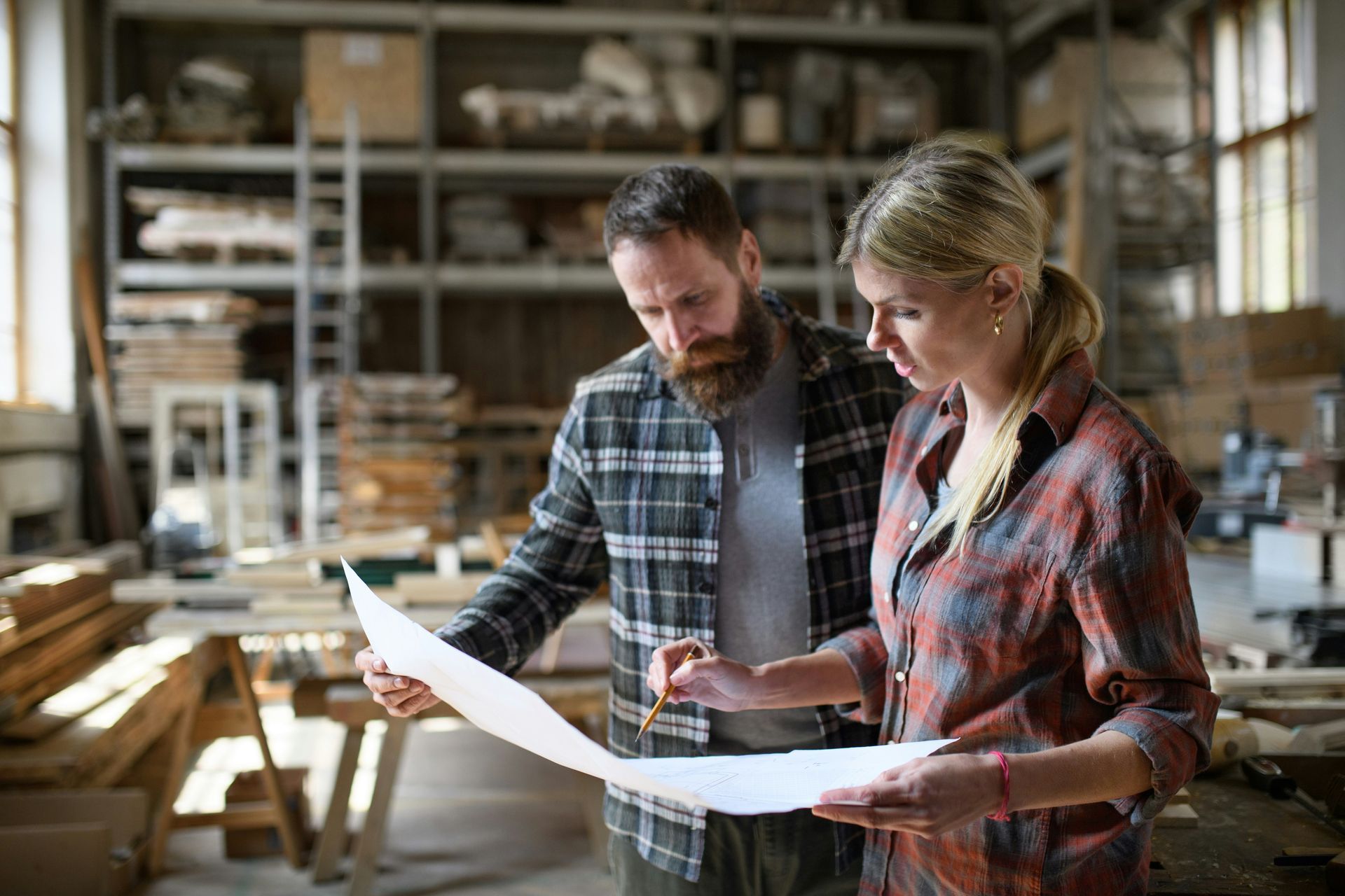 Two people reviewing plans together in a workshop, standing by a workbench with shelves in the background
