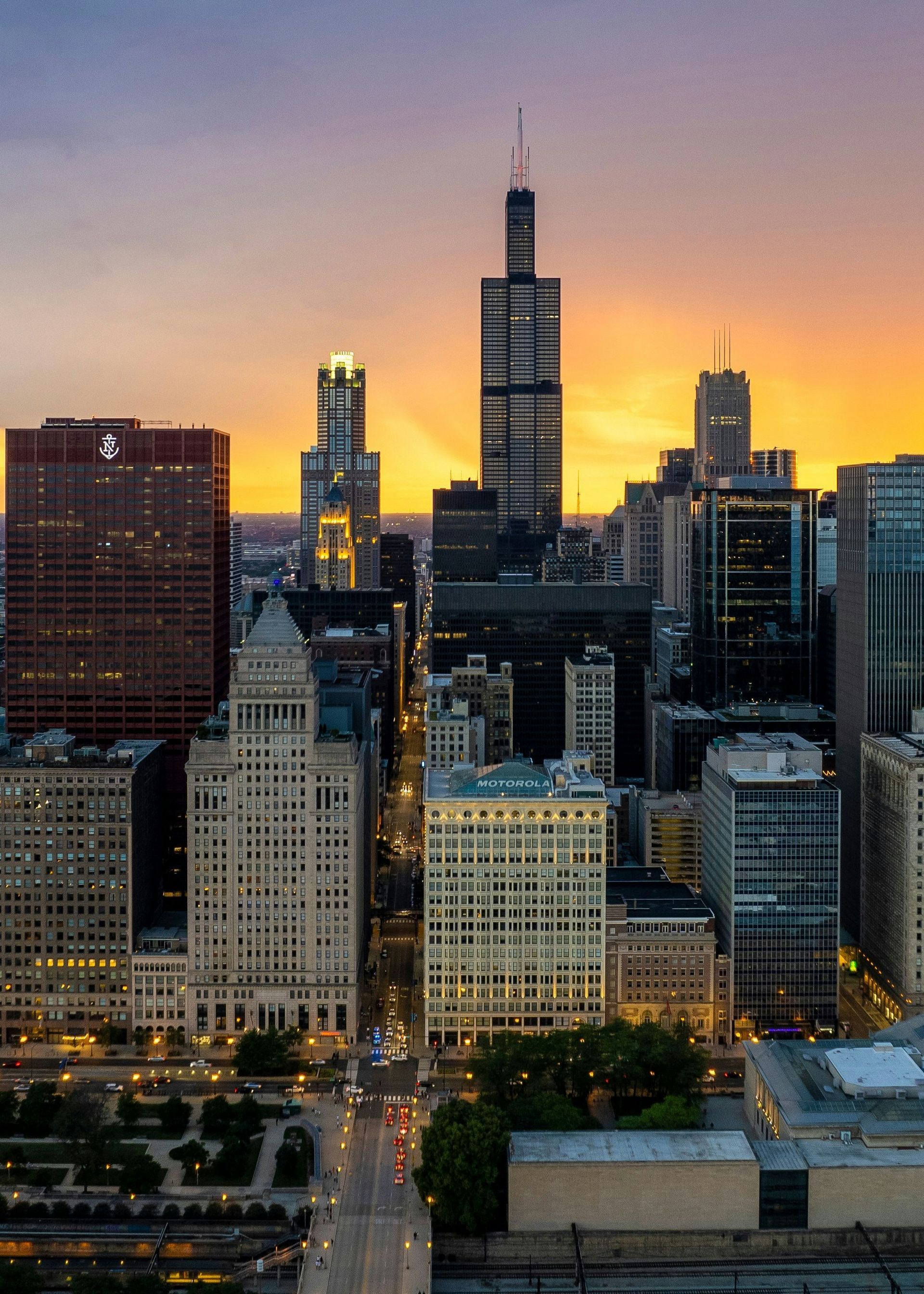 City skyline at sunset with a tall central skyscraper and glowing orange sky