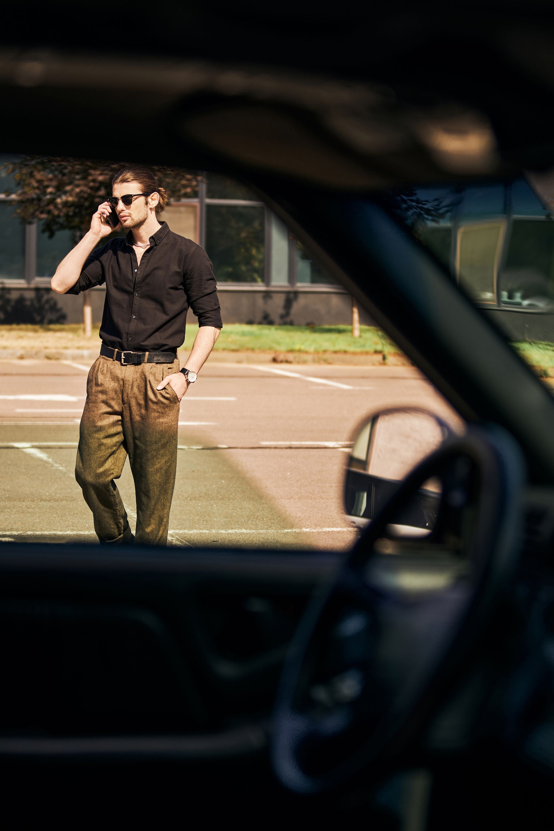 Man standing on a street, talking on a phone, seen through a car window