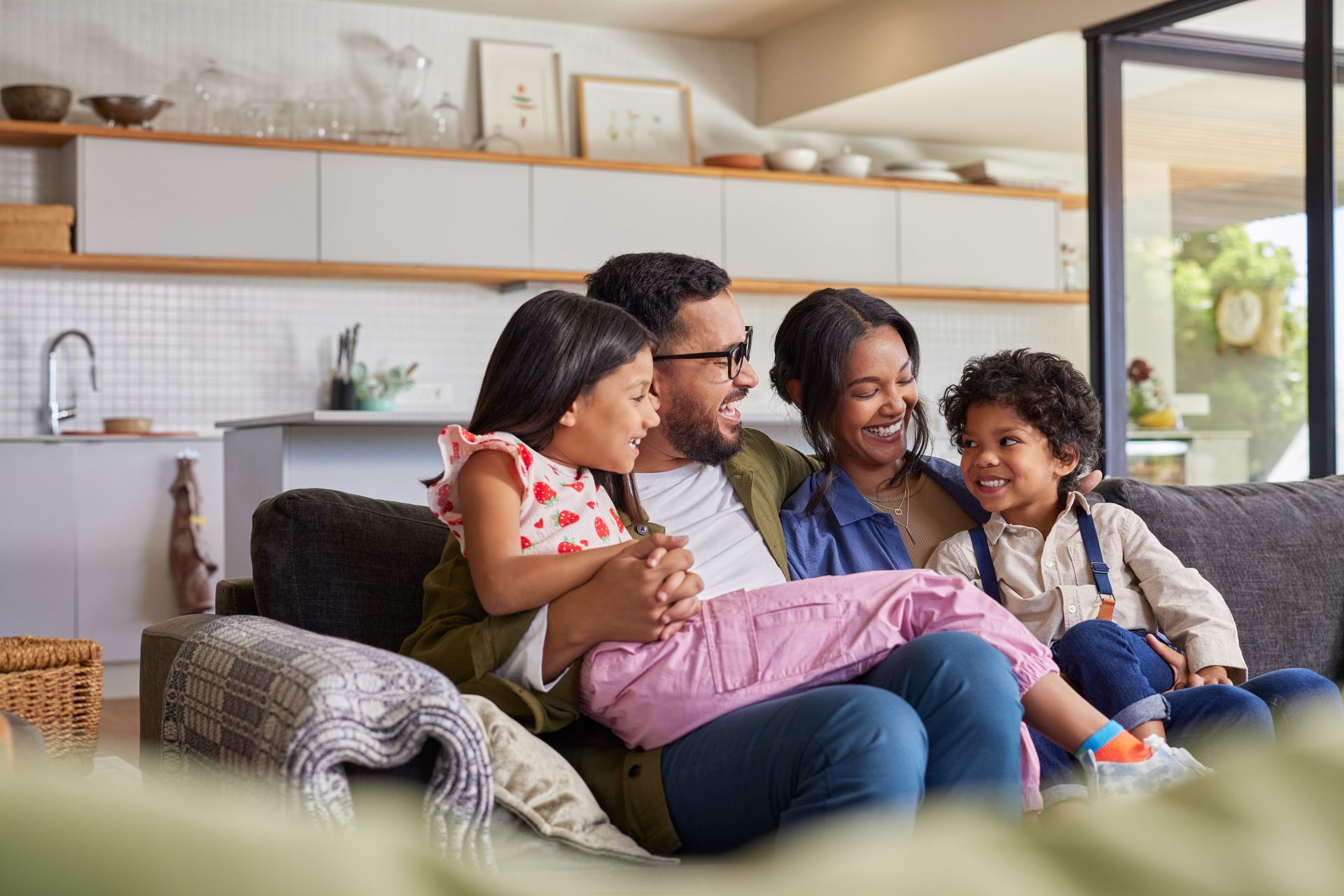 Family sitting together on a sofa in a bright living room, smiling and chatting