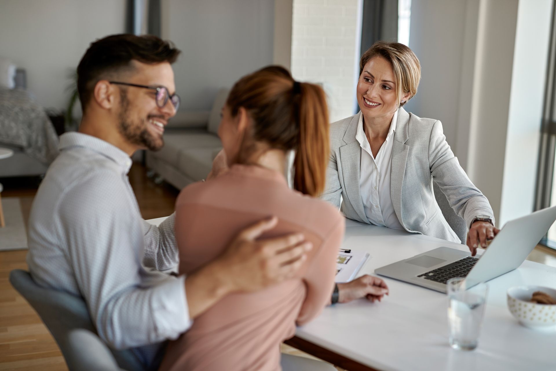 Three coworkers in a meeting at a white table, smiling and discussing a laptop