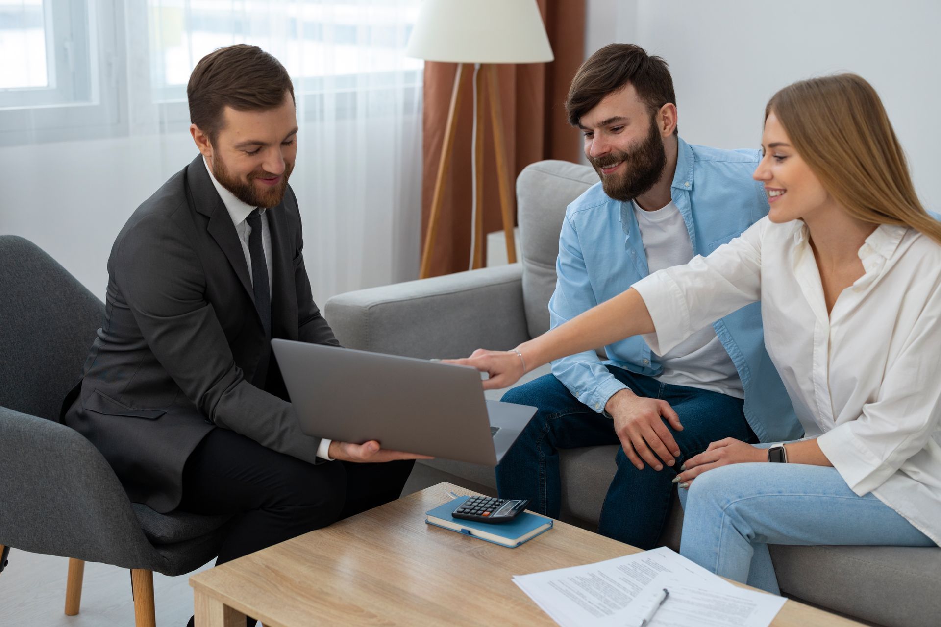 Three people reviewing documents on a couch with a laptop in a bright living room.